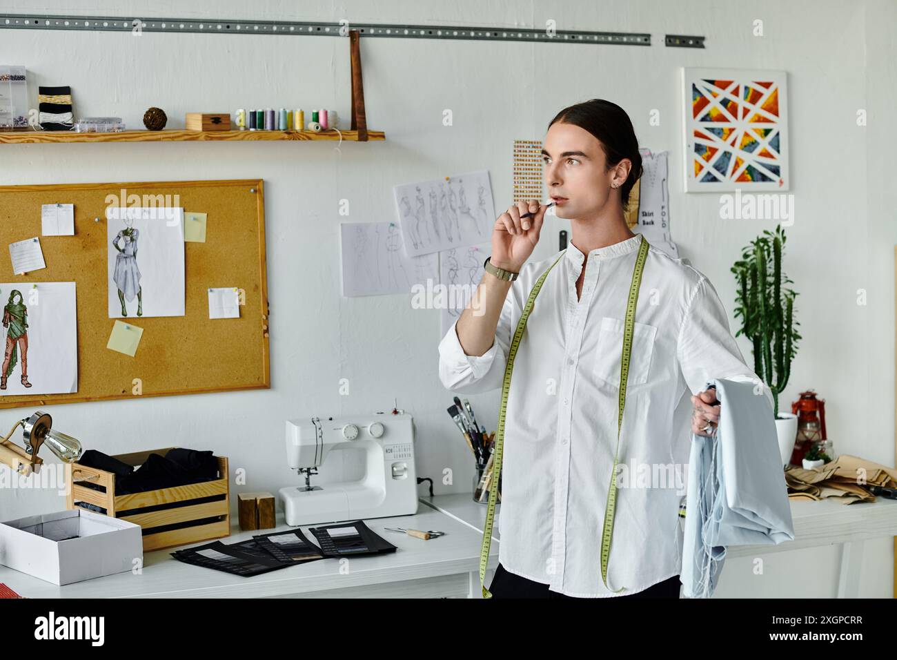 Un jeune homme se tient dans son atelier de restauration de vêtements, tenant soigneusement un morceau de tissu. Banque D'Images