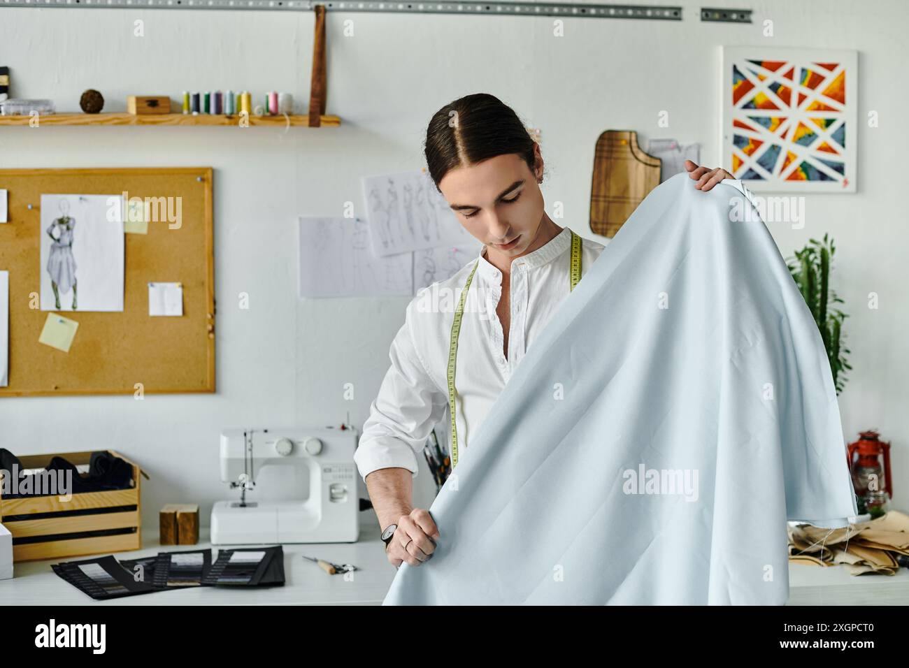 Un jeune homme en chemise blanche inspecte soigneusement le tissu dans son atelier de restauration de vêtements DIY. Il insuffle une nouvelle vie aux vêtements jetés, la promotine Banque D'Images