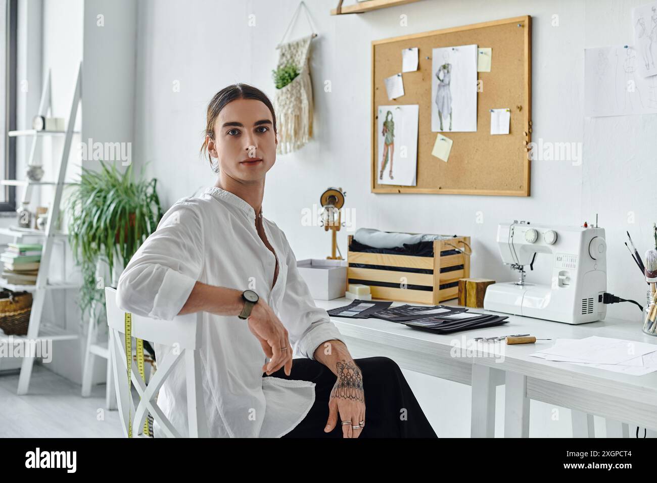 Un jeune homme est assis à son bureau dans son atelier de restauration de vêtements, montrant sa passion pour la mode durable. Banque D'Images
