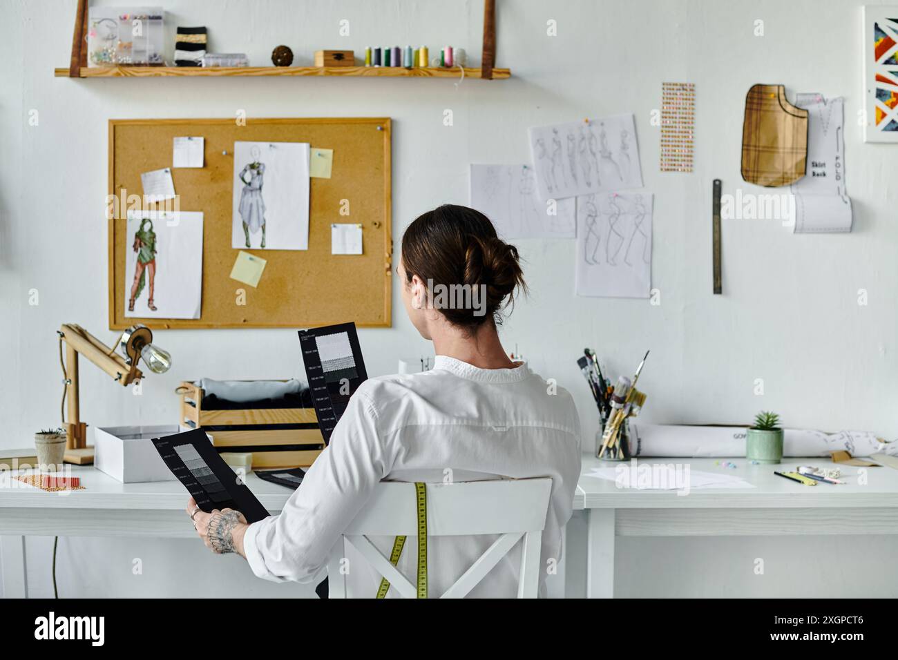 Un jeune homme, qui travaille dans son atelier de restauration de vêtements, examine soigneusement les échantillons de tissu assis à son bureau. Banque D'Images