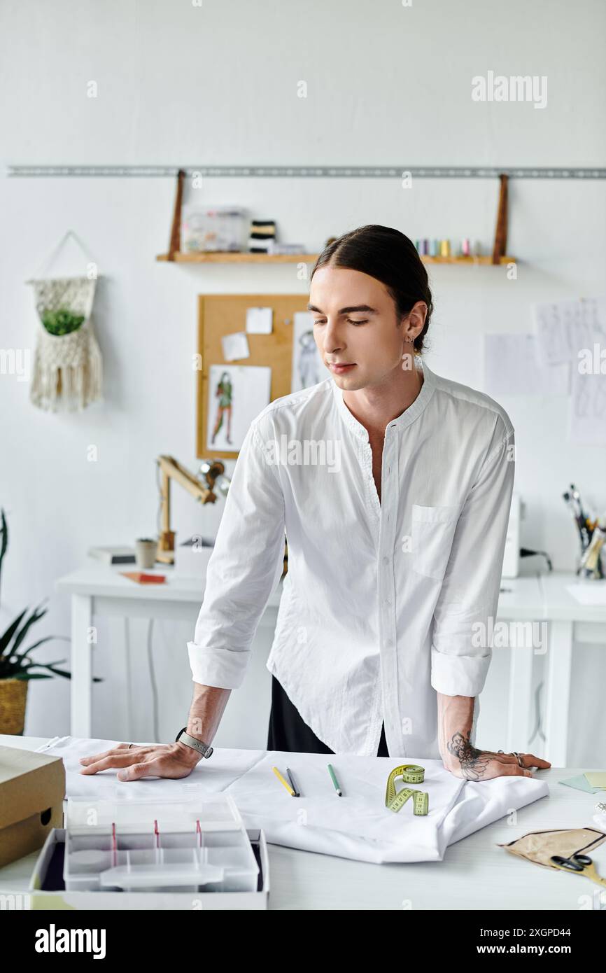 Un jeune homme en chemise blanche se tient dans son atelier de restauration de vêtements, concentré sur son travail. Banque D'Images