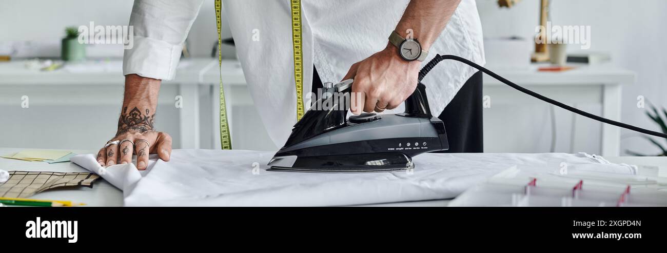 Un jeune homme en chemise blanche utilise un fer à repasser pour donner une nouvelle vie à des vêtements jetés. Banque D'Images