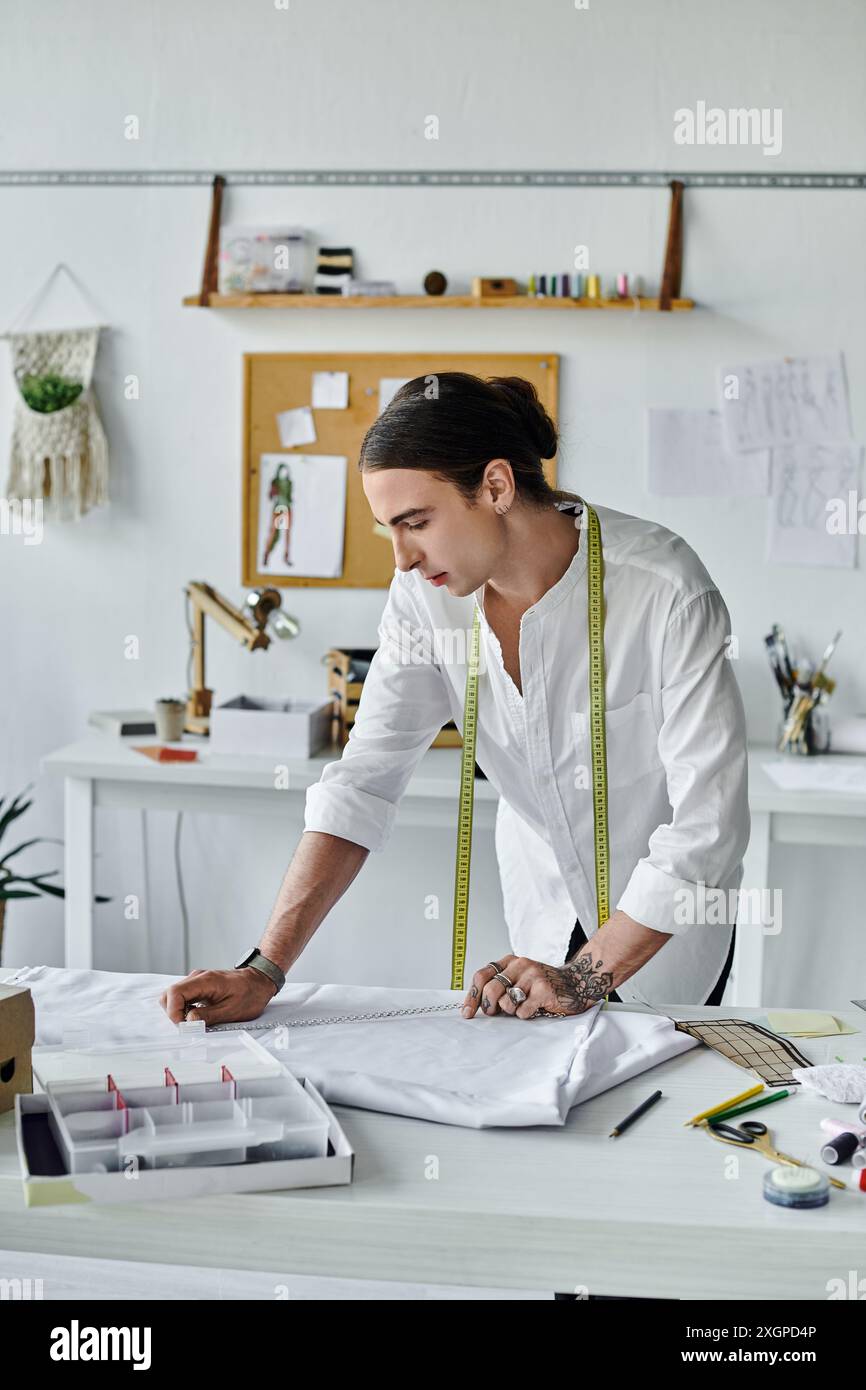 Un jeune homme en chemise blanche mesure méticuleusement le tissu dans son atelier de restauration de vêtements DIY, insufflant une nouvelle vie aux articles jetés. Banque D'Images