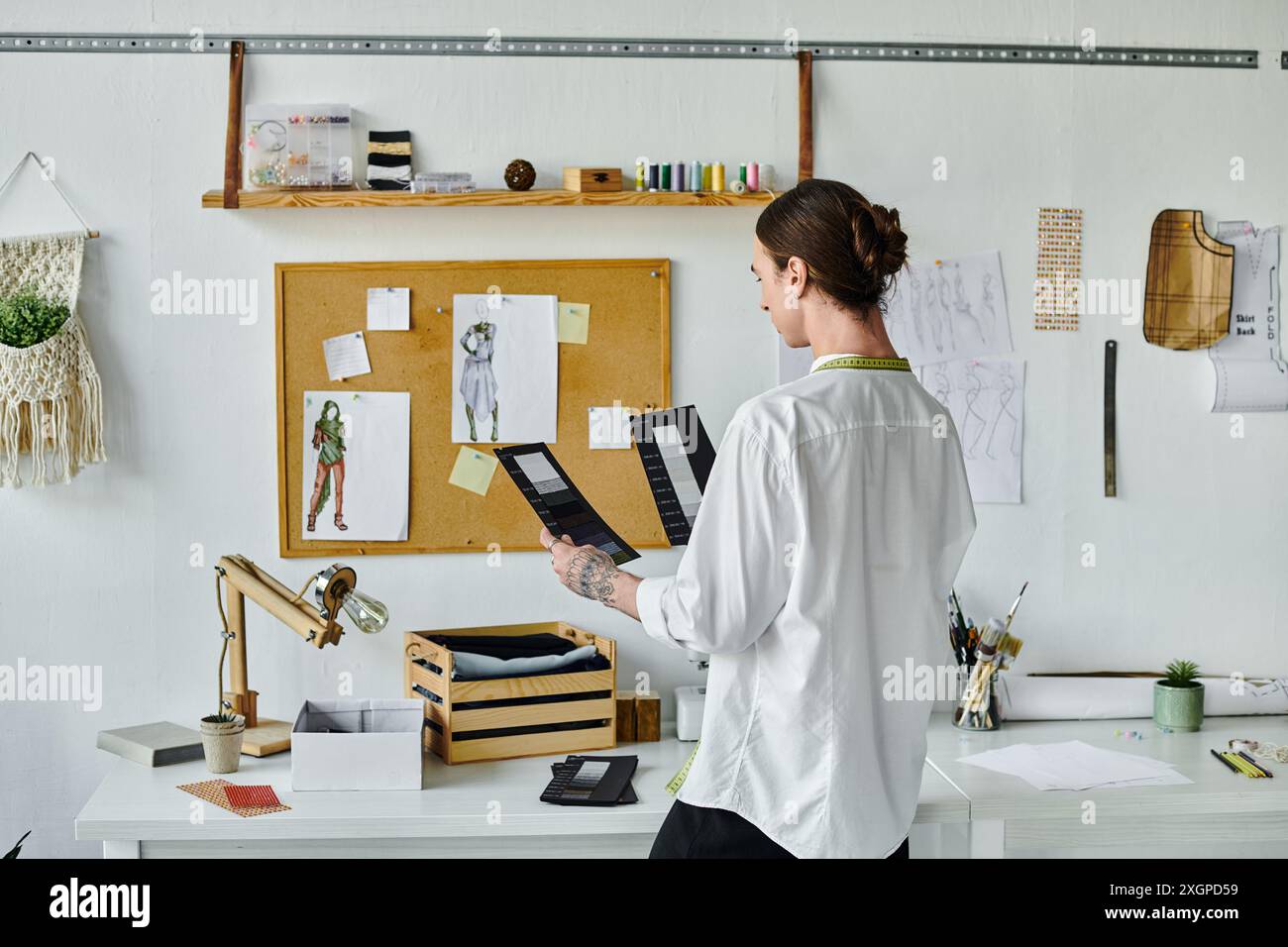 Un jeune homme en chemise blanche se tient debout dans son atelier de restauration de vêtements DIY, tenant des échantillons de tissu, démontrant son engagement envers la durabilité A. Banque D'Images
