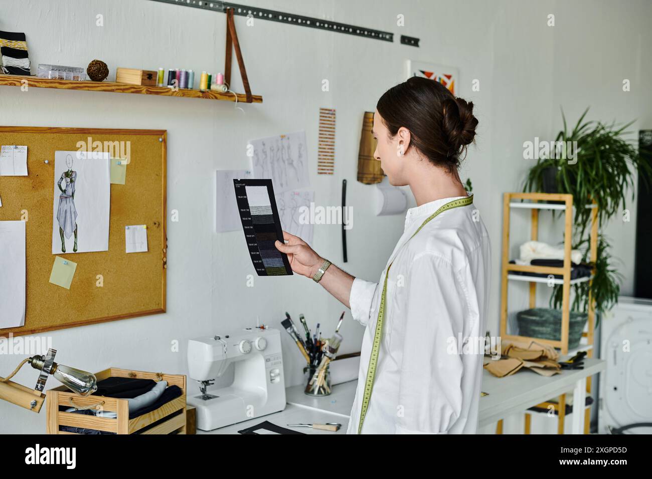Un jeune homme, vêtu de blanc, examine des échantillons de tissu dans son atelier de couture, démontrant une passion pour la restauration durable des vêtements. Banque D'Images