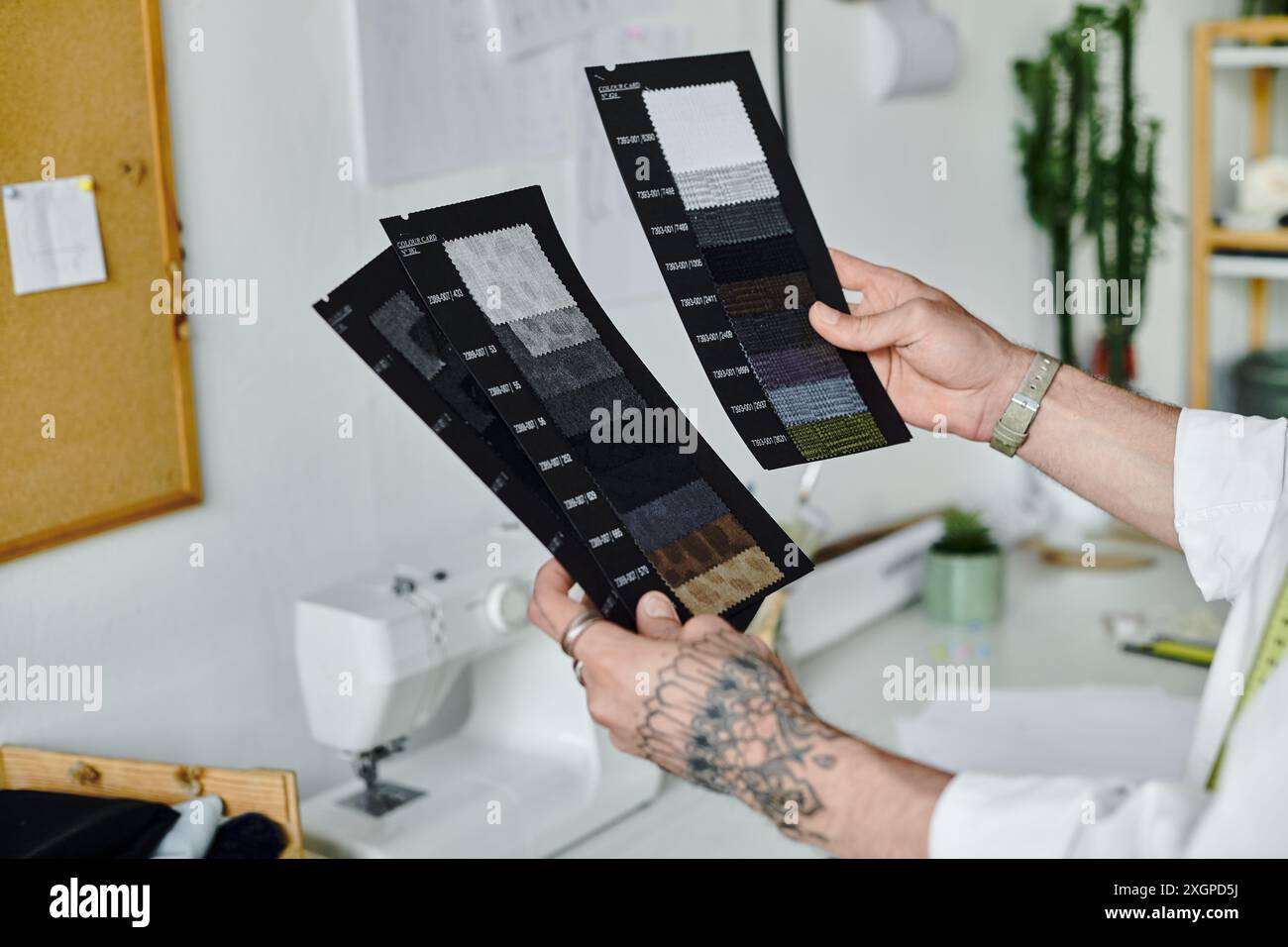 Un jeune homme en chemise blanche examine des échantillons de tissu dans son atelier de restauration de vêtements. Banque D'Images