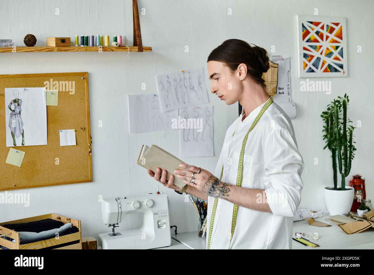 Un jeune homme en chemise blanche se tient dans son atelier, examinant des croquis tout en tenant un livre. Banque D'Images