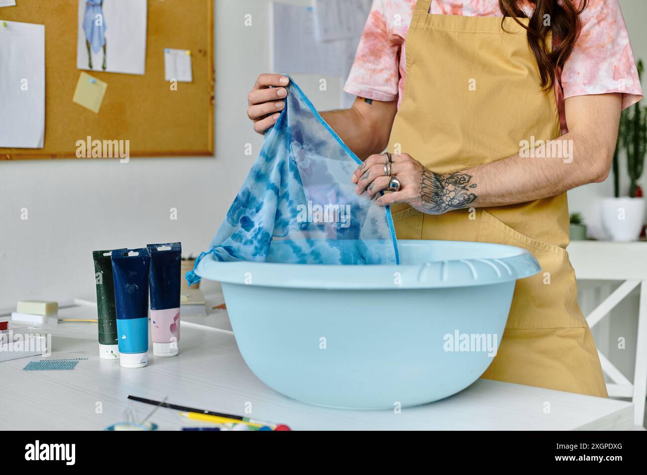 Un jeune homme teint un tissu dans un bassin, dans le cadre de son atelier de restauration de vêtements durables. Banque D'Images