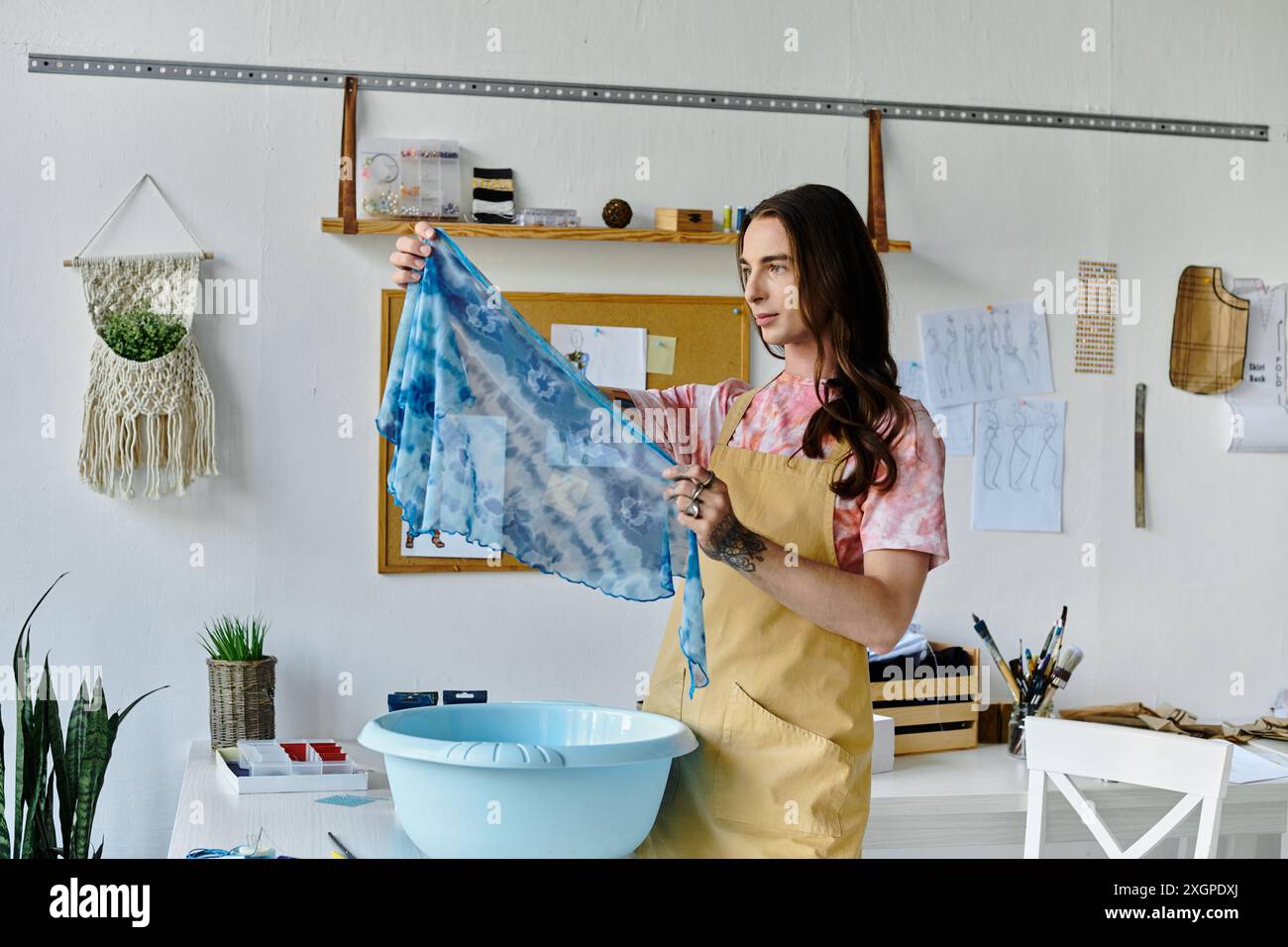 Un jeune homme examine un morceau de tissu teint au noeud qu’il restaure dans son atelier de vêtements, en se concentrant sur la durabilité et en donnant une nouvelle vie à des articles anciens. Banque D'Images