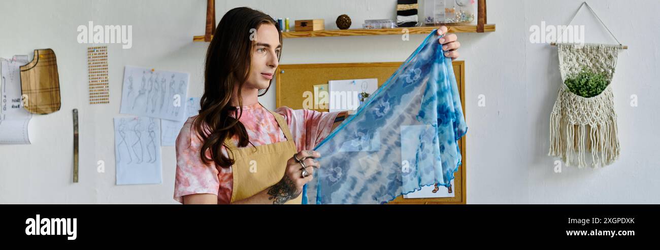 Un jeune homme dans un t-shirt rose clair et un tablier tient un tissu bleu et blanc vif teint dans son atelier de restauration de vêtements. Banque D'Images