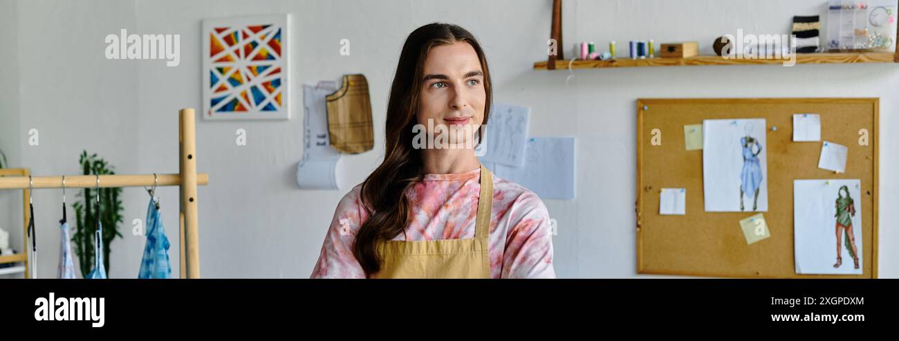 Un jeune homme, portant un tablier, se tient dans son atelier de restauration de vêtements, axé sur la redynamisation des vêtements jetés. Banque D'Images