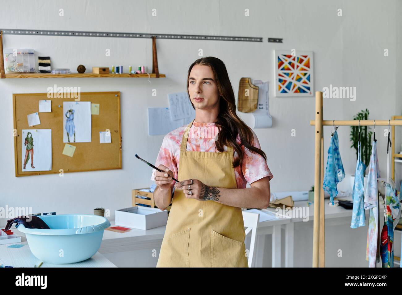 Un jeune homme se tient dans son atelier de restauration de vêtements, tenant un pinceau, entouré de son travail créatif. Banque D'Images