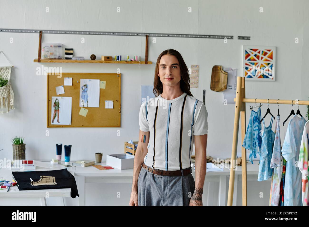 Un jeune homme gay se tient dans son atelier de restauration de vêtements, montrant son engagement envers la mode durable en donnant une nouvelle vie aux vieux vêtements. Banque D'Images
