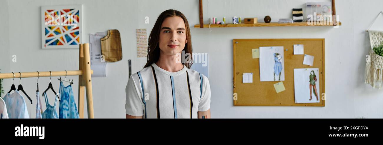Un jeune homme gsy se tient dans son atelier de restauration de vêtements, entouré de tissus colorés et d’inspiration design. Banque D'Images