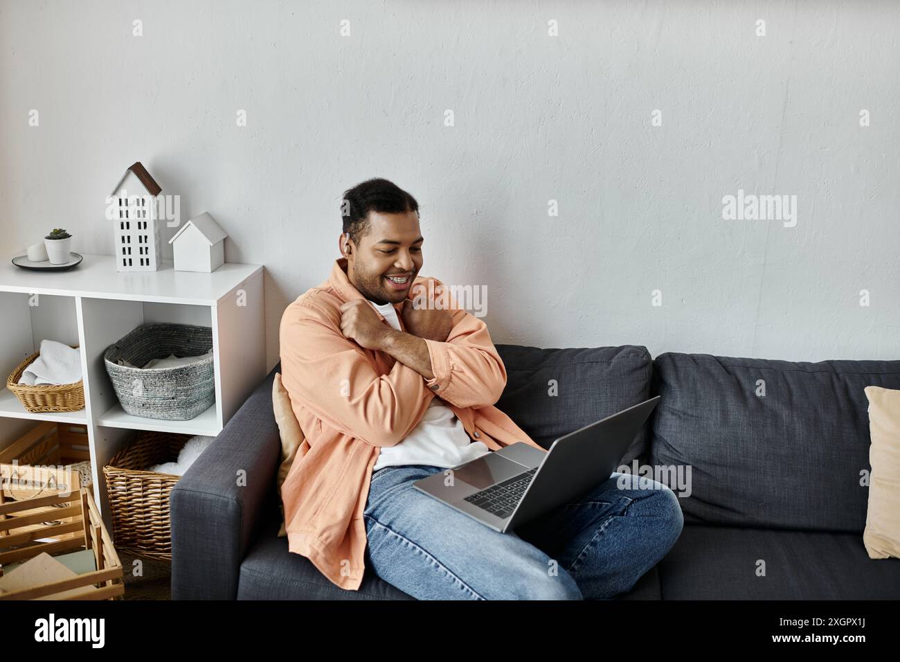 Un homme afro-américain assis sur un canapé, souriant et communiquant en utilisant la langue des signes. Banque D'Images