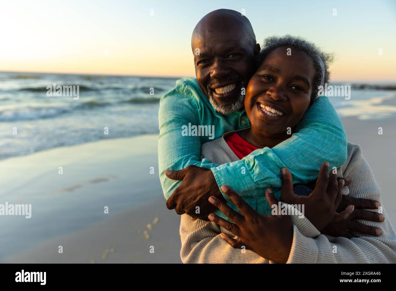 Couple senior afro-américain profite d'une étreinte au coucher du soleil sur la plage. Leur moment joyeux capture un cadre extérieur romantique. Banque D'Images