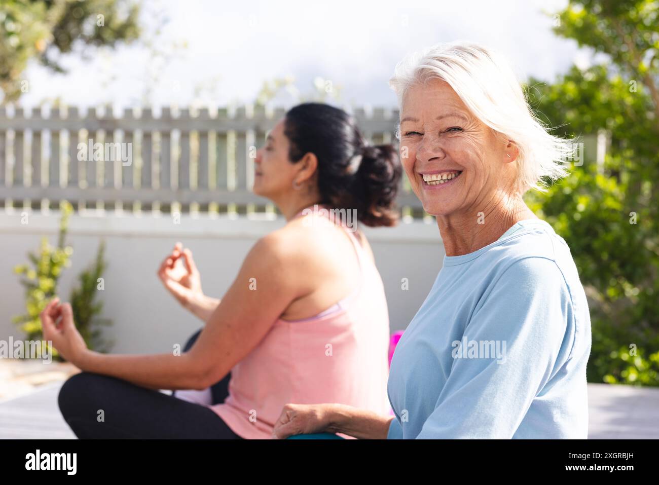 Heureuses amies seniors diverses pratiquant la méditation yoga assise dans un jardin ensoleillé. Lotus position, yoga, bien-être, méditation, amitié et lui Banque D'Images