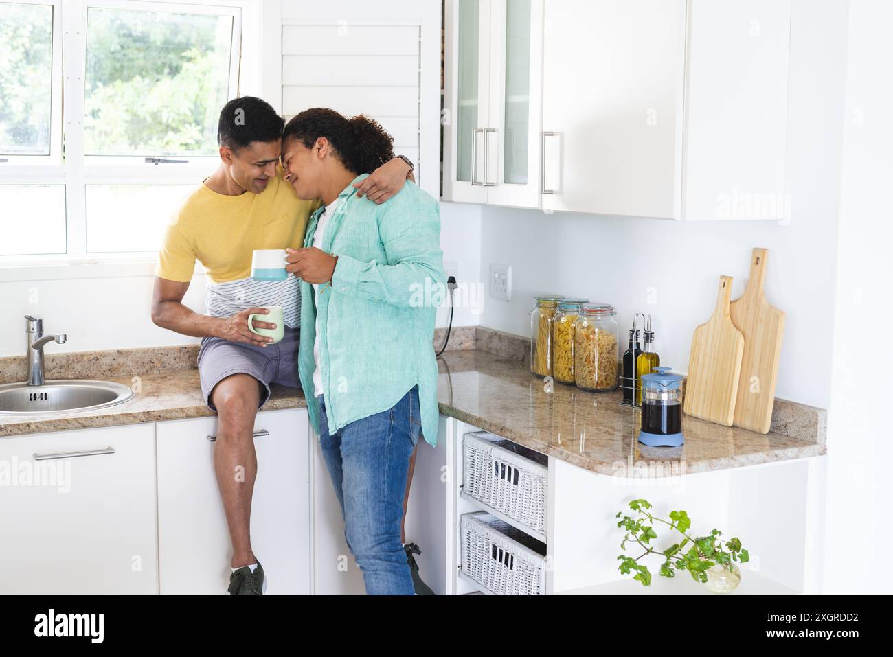 Couple biracial gay partageant un moment dans une cuisine lumineuse. Ils profitent d'une matinée confortable ensemble, rayonnant de chaleur et d'affection. Banque D'Images
