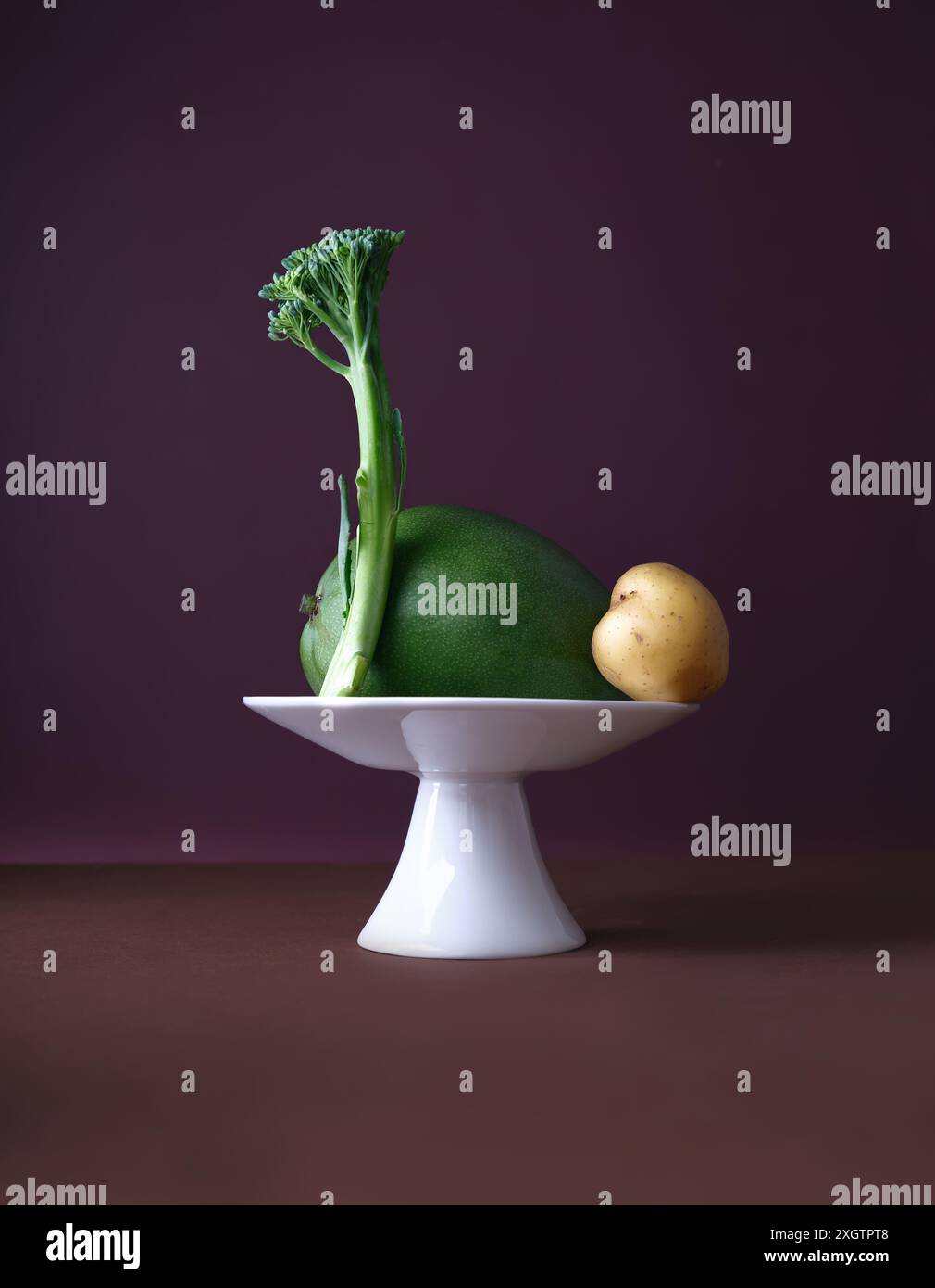 Un présentoir créatif avec une tige de mangue, de pomme de terre et de brocoli agencée habilement sur un petit piédestal blanc élégant sur un fond violet riche Banque D'Images