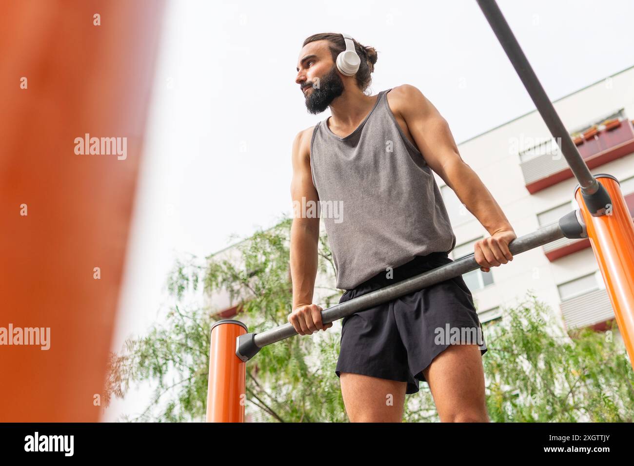 Angle bas de jeune homme concentré avec une barbe s'entraîne dans un parc de fitness en plein air à Poblenou, écoutant de la musique à travers son casque, enhancin Banque D'Images