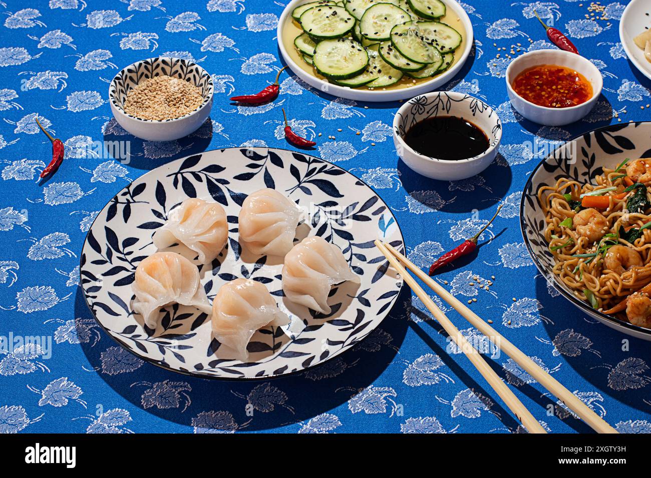 Cuisine chinoise variée, avec boulettes, concombres au vinaigre, sauces épicées et nouilles sautées, joliment arrangé sur un flo bleu Banque D'Images