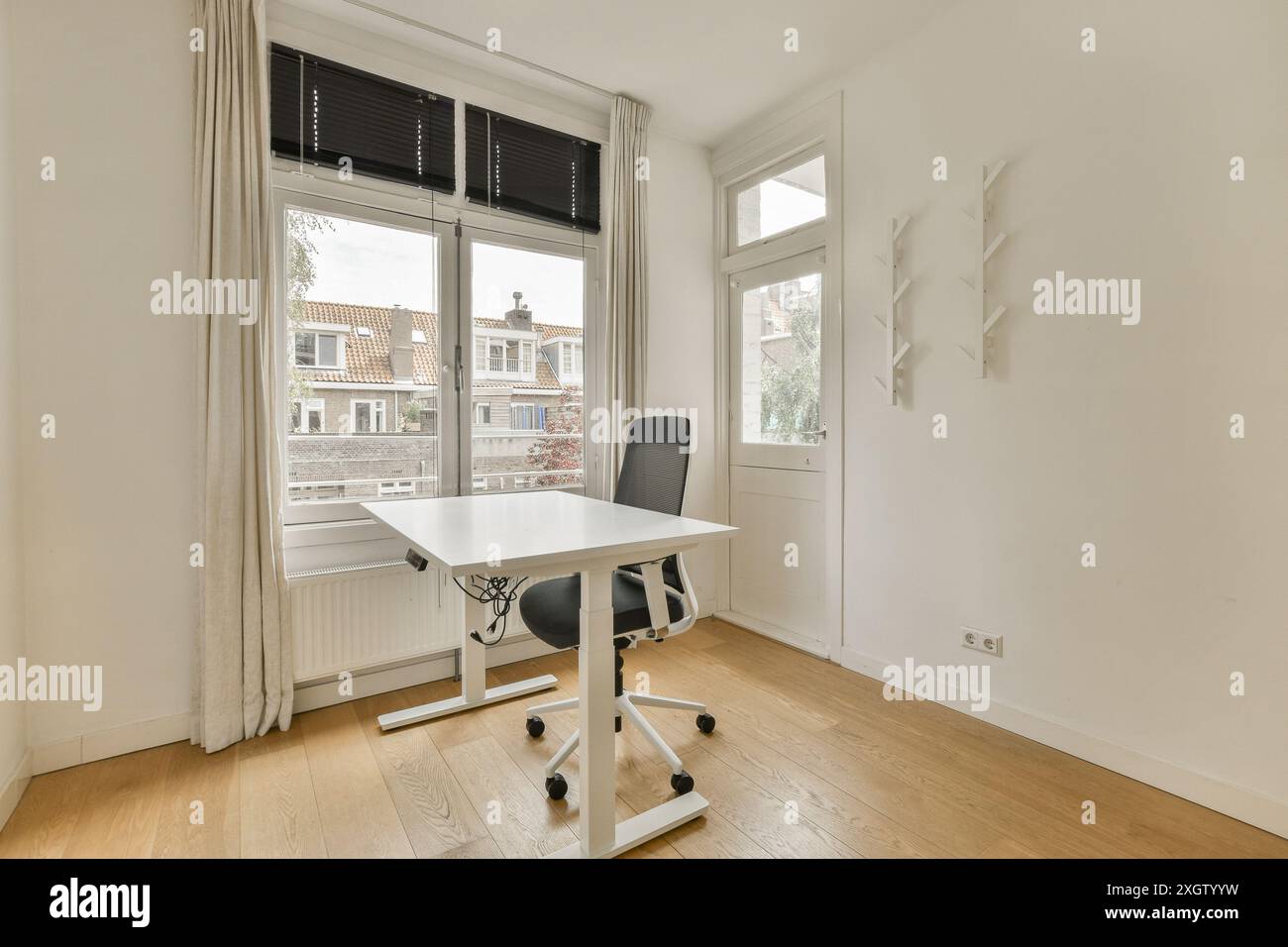 Un bureau à domicile moderne et lumineux au style minimaliste, avec un bureau blanc, une chaise de bureau et des stores. Banque D'Images