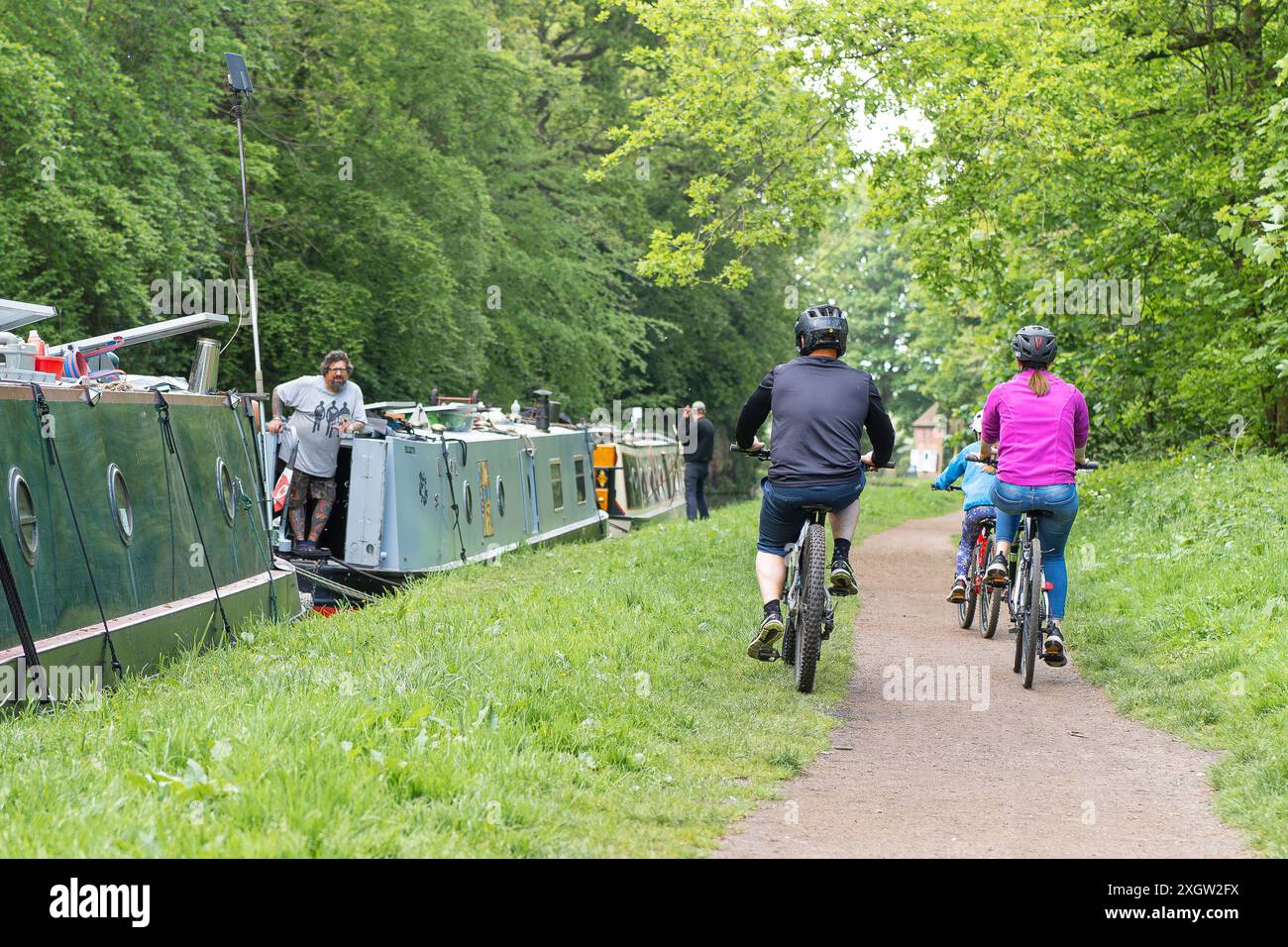 Vue arrière d'une famille cyclant le long d'un chemin de halage du canal britannique portant des casques de cyclisme de sécurité. Banque D'Images