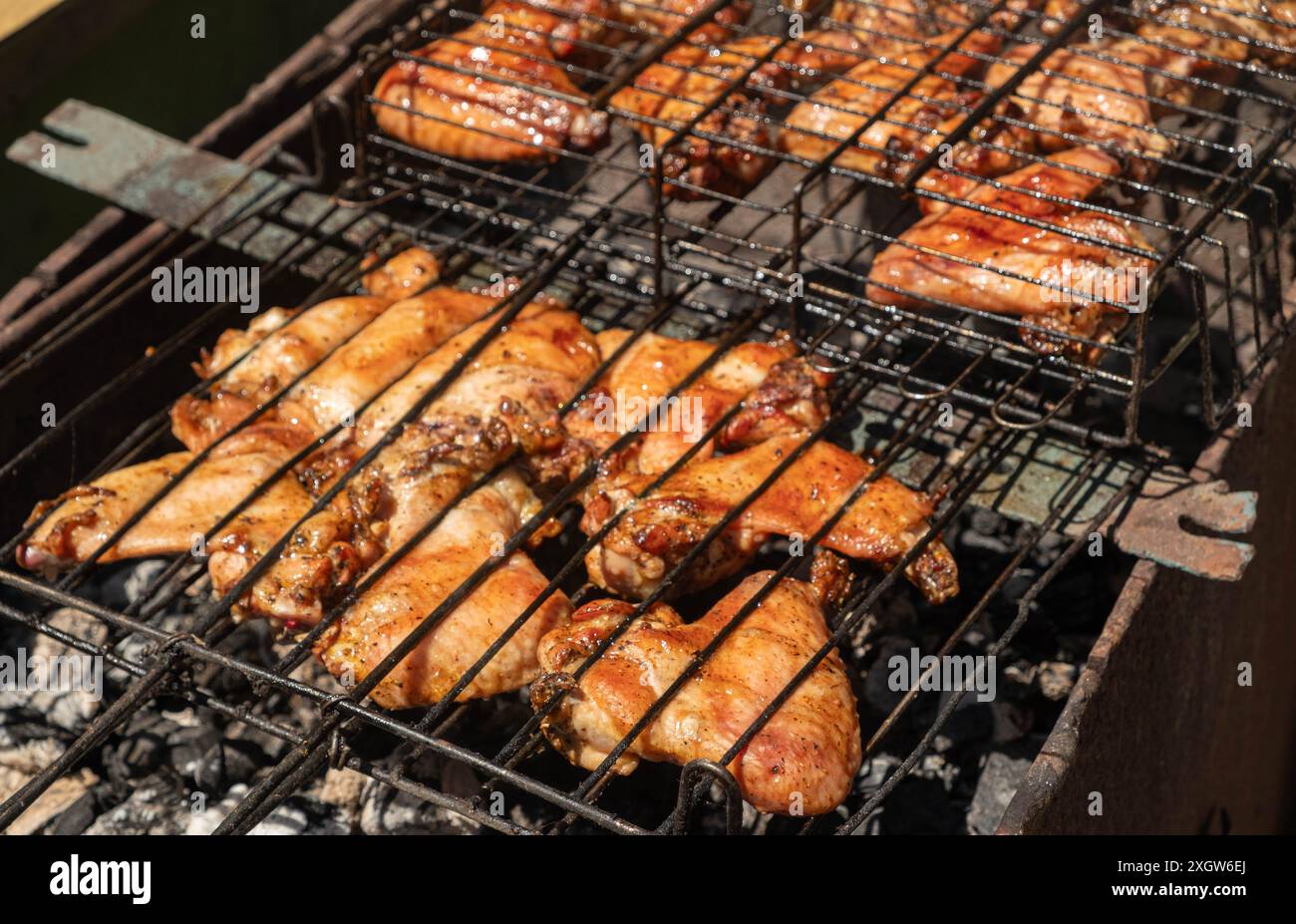 Gros plan de succulents morceaux de poulet assaisonnés grillés sur un barbecue sur des charbons, capturant la saveur délicieuse et fumée de la cuisine en extérieur. Banque D'Images