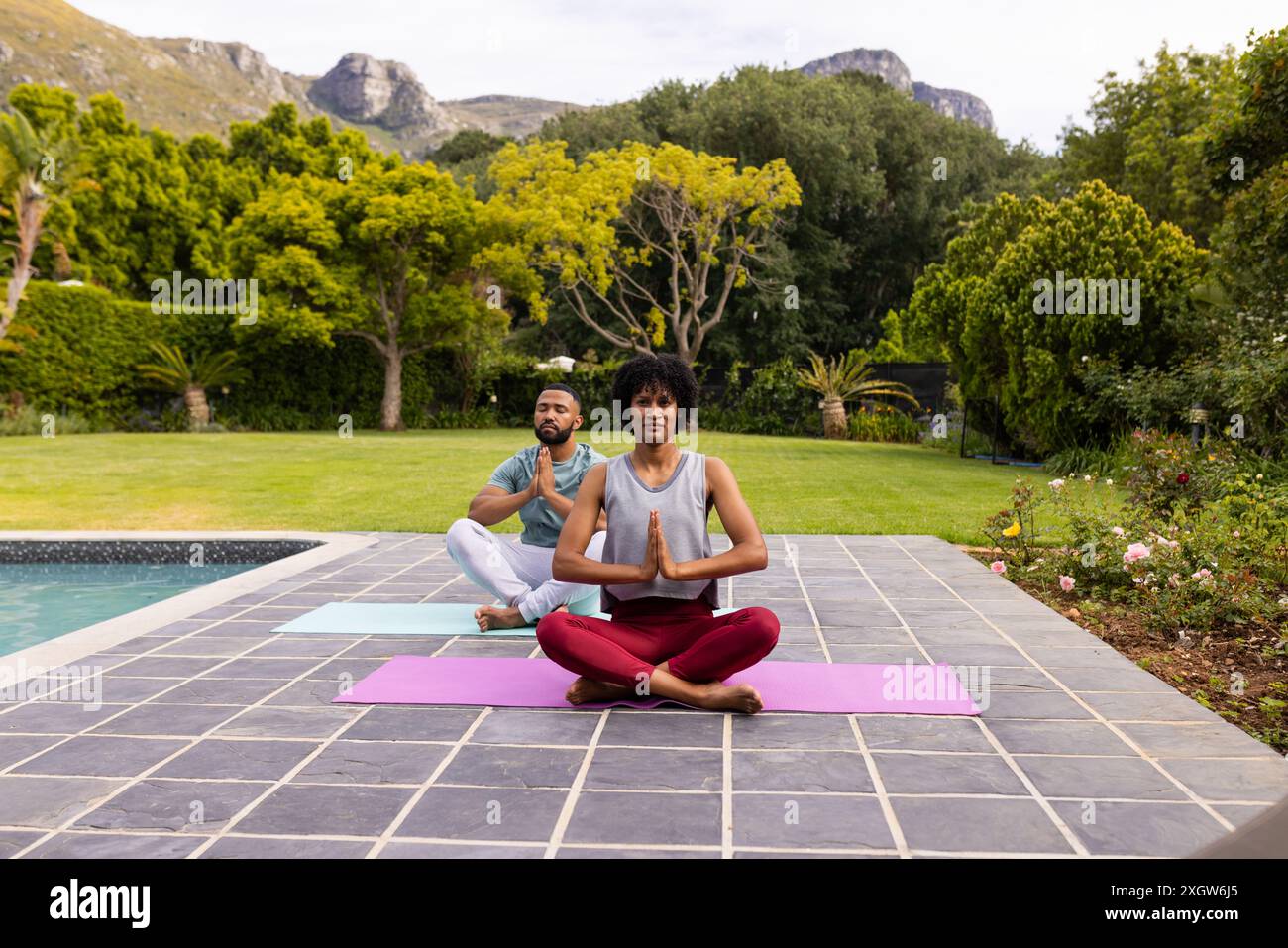 Couple biracial pratiquant le yoga en plein air, avec espace de copie. Ils profitent d'une séance sereine au bord de la piscine entourée par la nature. Banque D'Images