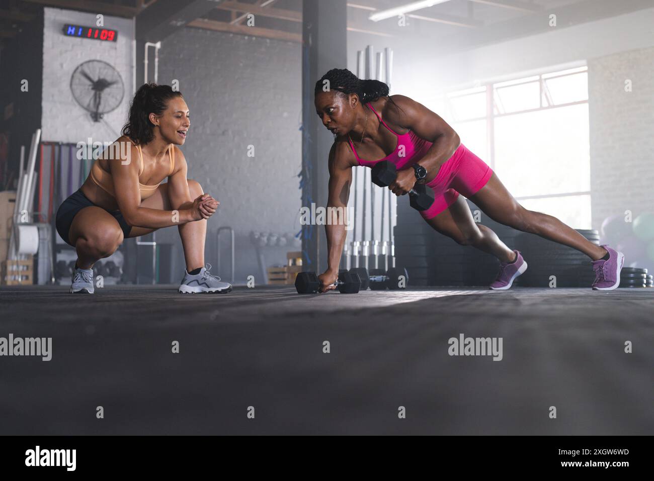 Femmes biraciales fortes et en forme exerçant dans un gymnase. Ils maintiennent la concentration et la détermination pendant leur routine de remise en forme. Banque D'Images