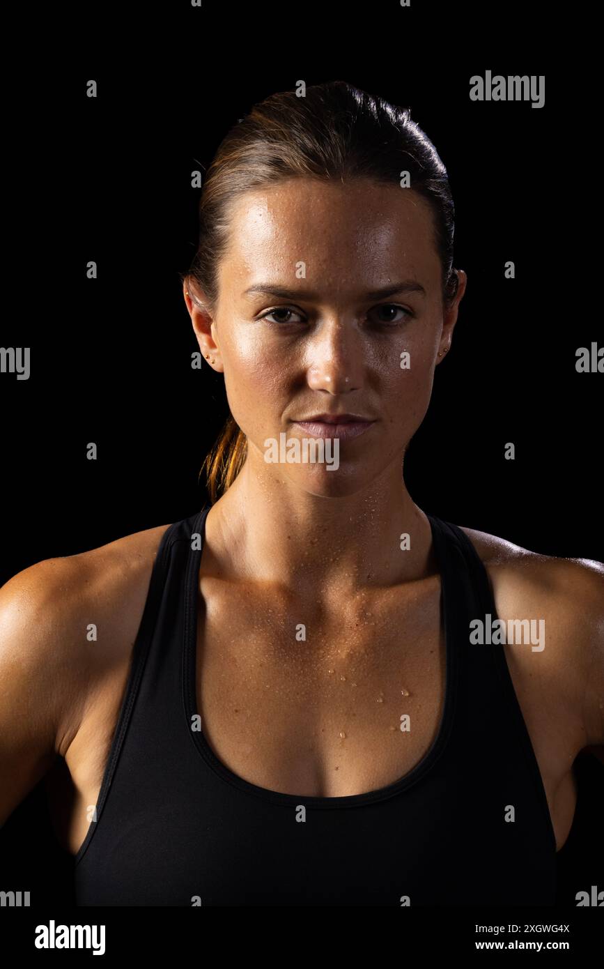 Déterminée jeune athlète féminine caucasienne est prête pour une séance d'entraînement sur un fond noir. Son regard intense et sa tenue athlétique suggèrent une focalisation sur la fi Banque D'Images