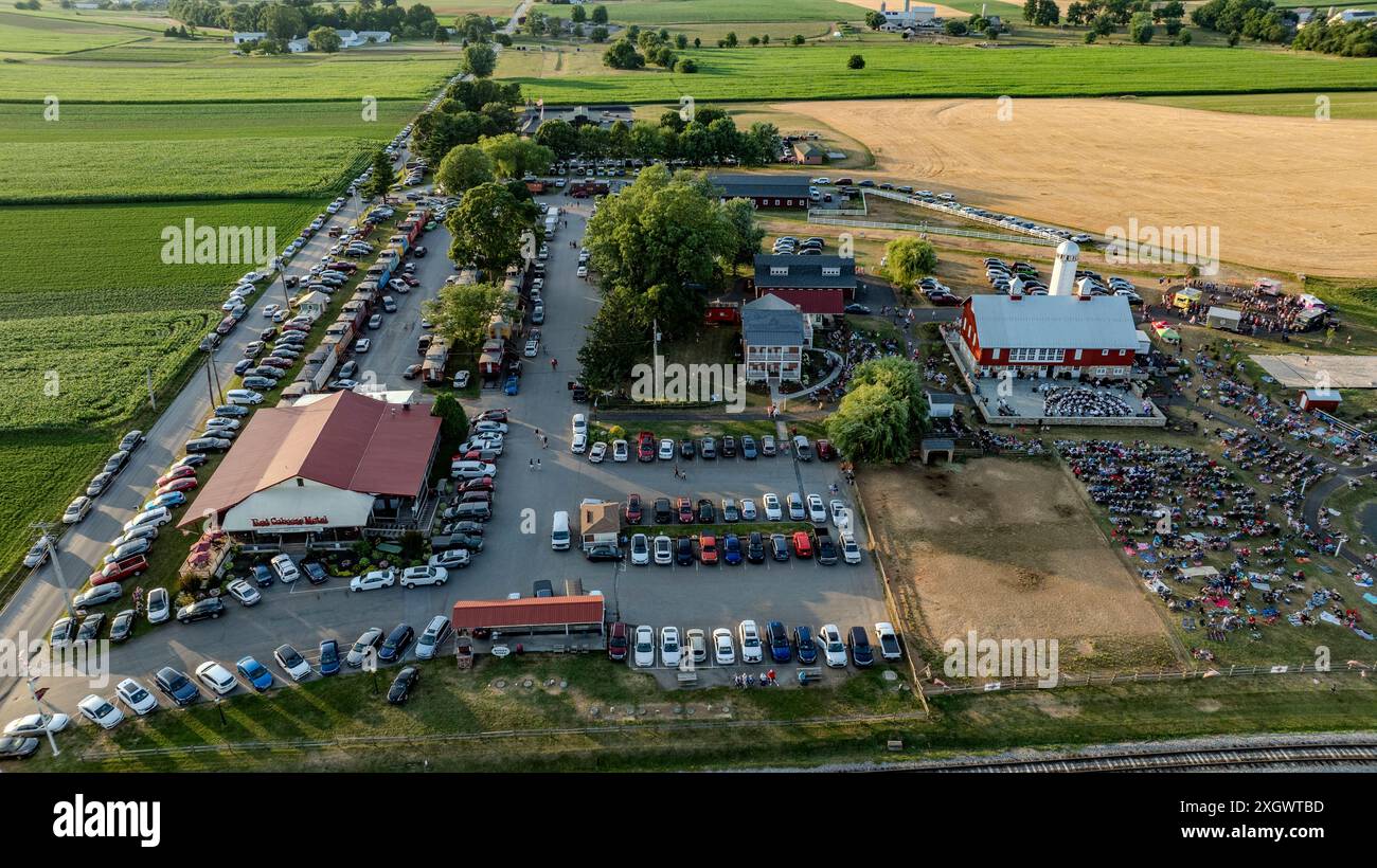 Ronks, Pennsylvanie, États-Unis, 3 juillet 2024 - vue aérienne d'Un événement agricole mettant en vedette Une grange rouge, un silo, une foule, des camions de nourriture, un grand parking, et les champs environnants avec des pistes de chemin de fer à proximité. Banque D'Images