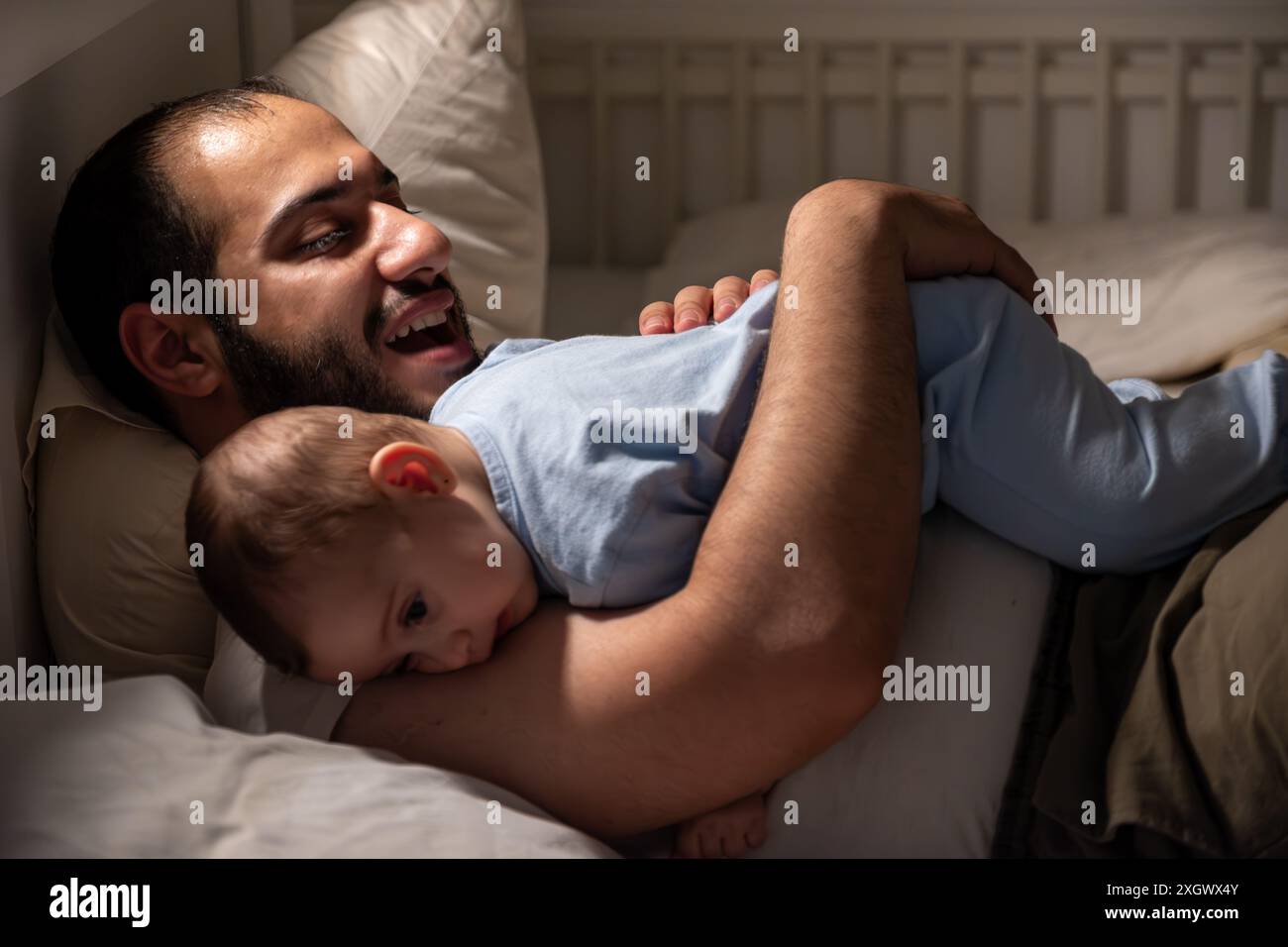 Père prend soin de son nouveau-né alors qu'il ne peut pas dormir la nuit sur le lit avec une faible lumière jaune, difficile à dormir ou ne peut pas dormir Banque D'Images