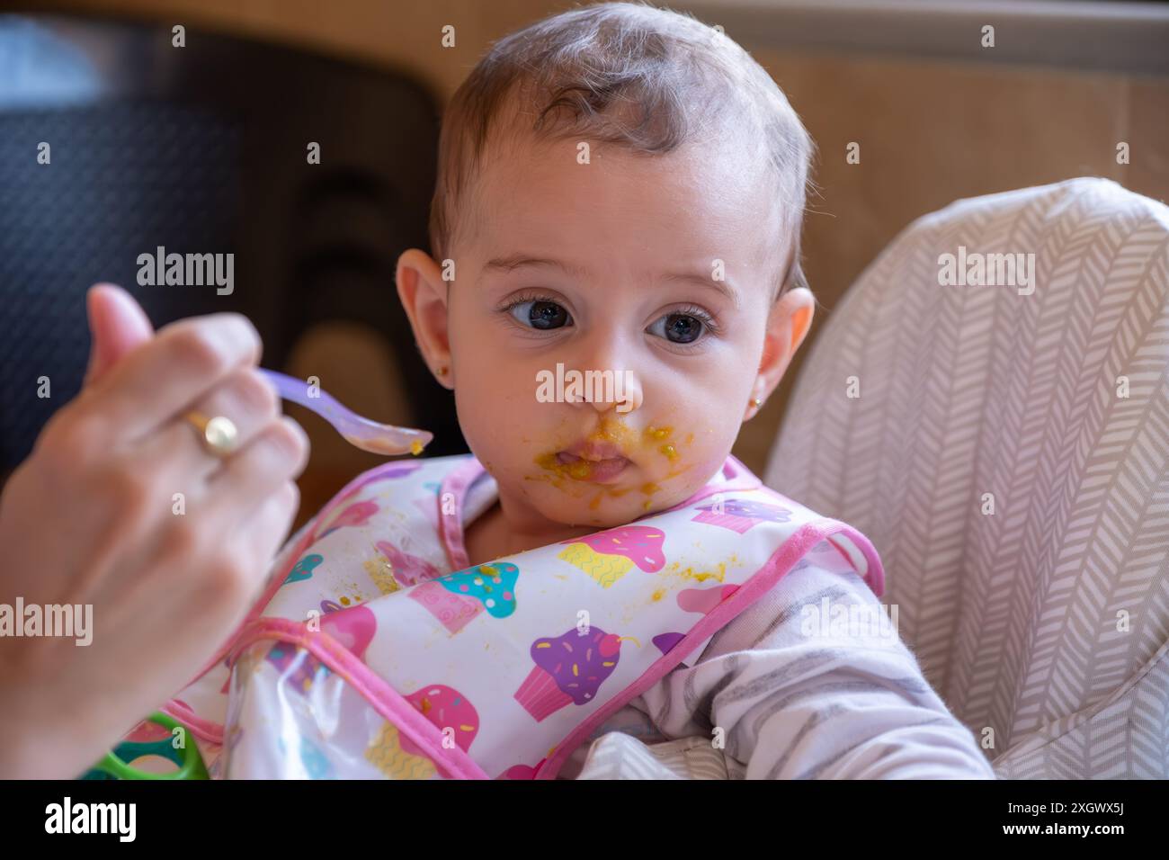 Un enfant est sur une chaise haute et la mère essaie de le nourrir, et son visage a des expressions de refus de manger, de distraction et de détournement du regard. Alimentation Banque D'Images
