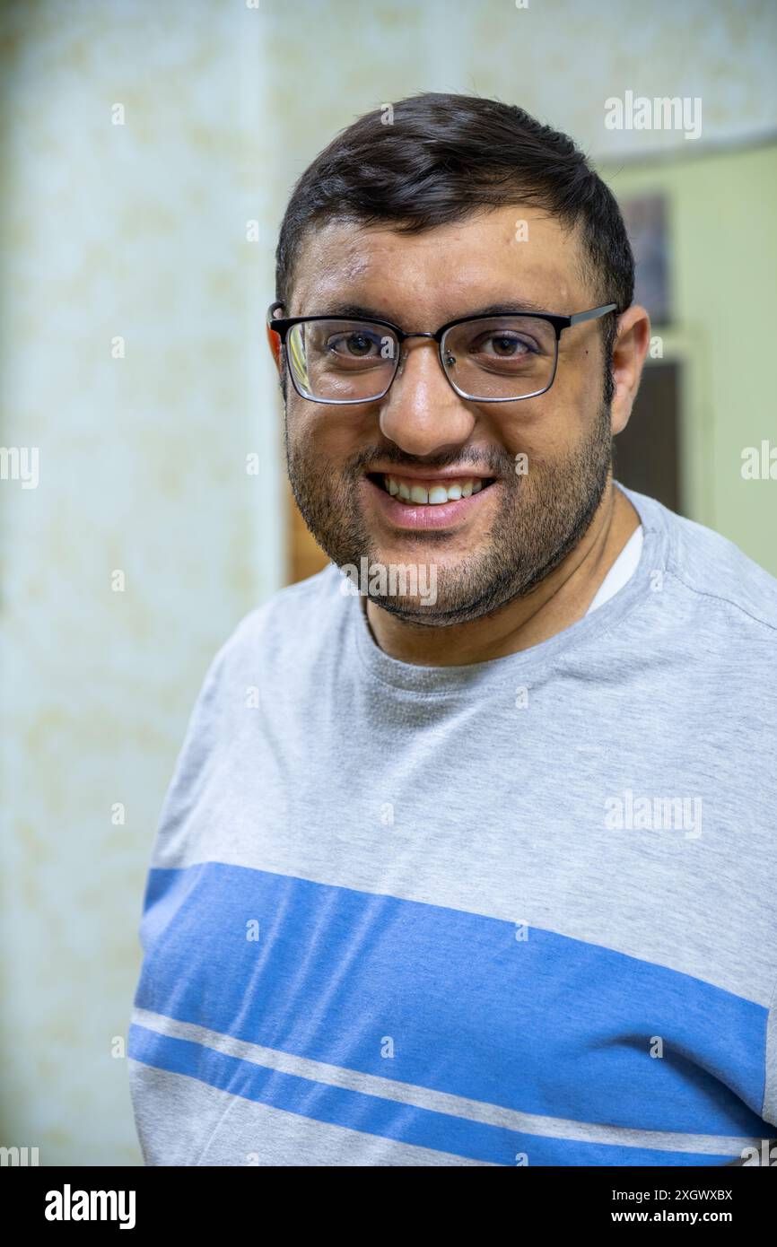 Homme en lunettes, souriant et détendu à la maison, capturé dans des portraits francs. Assis sur un fauteuil, portant des chemises décontractées. Parfait pour le style de vie et ev Banque D'Images