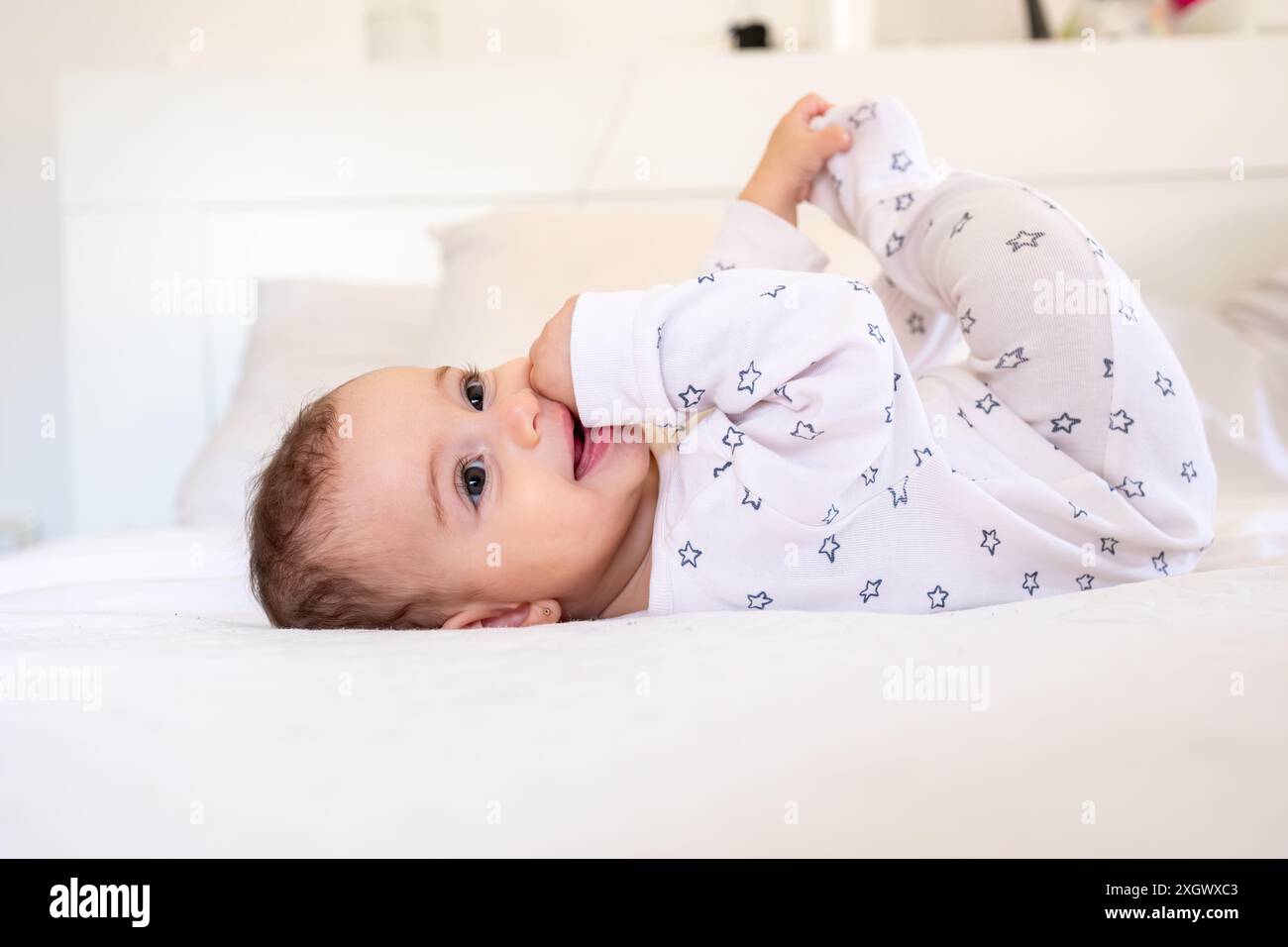 Mignon petit bébé blanc drôle s'amuser tout en étant allongé sur le lit à la maison, adorable arabian Infant Girl jouant avec ici orteils et riant tout en se reposant dedans Banque D'Images