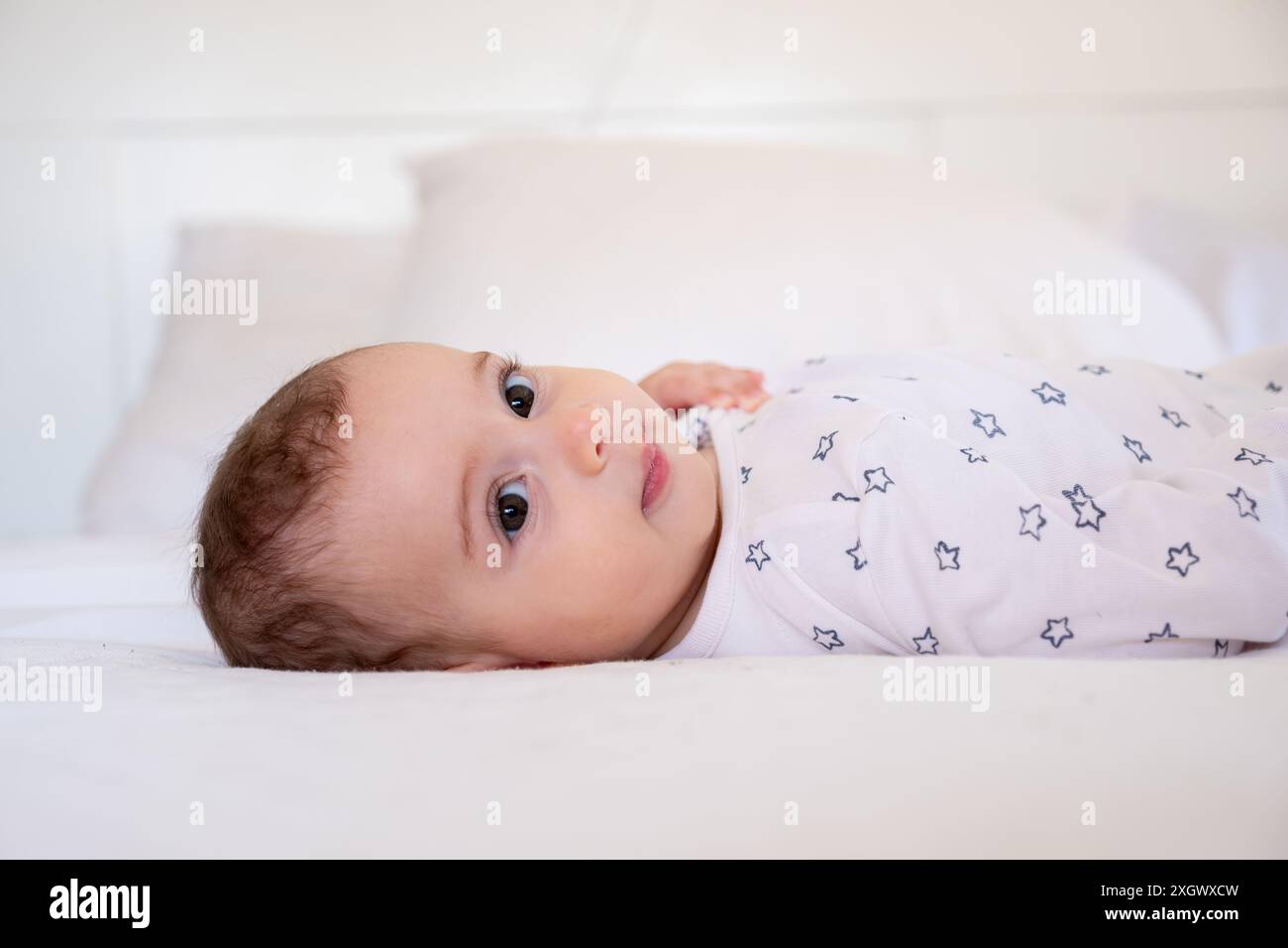 Mignon petit bébé blanc drôle s'amuser tout en étant allongé sur le lit à la maison, adorable arabian Infant Girl jouant avec ici orteils et riant tout en se reposant dedans Banque D'Images