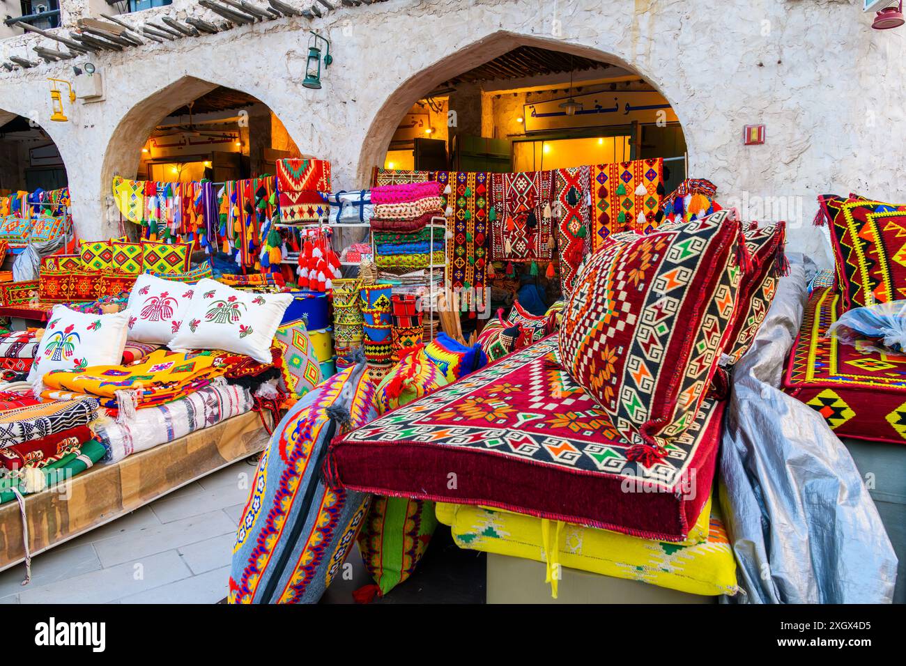 Une vitrine extérieure colorée vendant des tissus aux couleurs vives sur des couvertures, des tapis et des oreillers sur le marché Souq Waqif de Doha Qatar. Banque D'Images