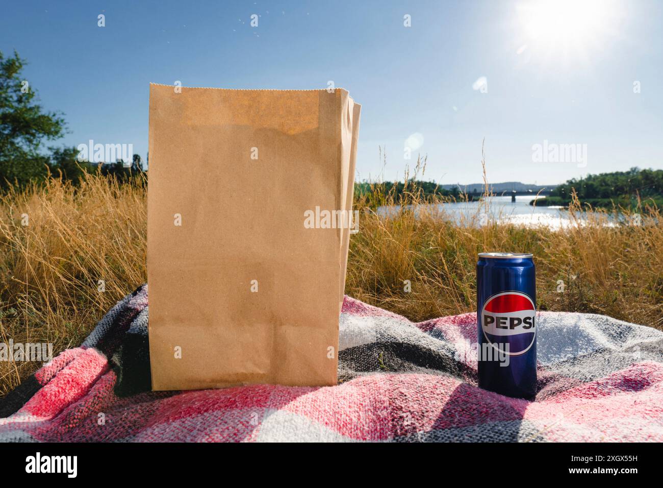 Krivoy Rog, Ukraine, 26 juin 2024 : une boîte de Pepsi-Cola et un sac en papier jetable reposent sur une couverture sur la rive de la rivière (gros plan) Banque D'Images