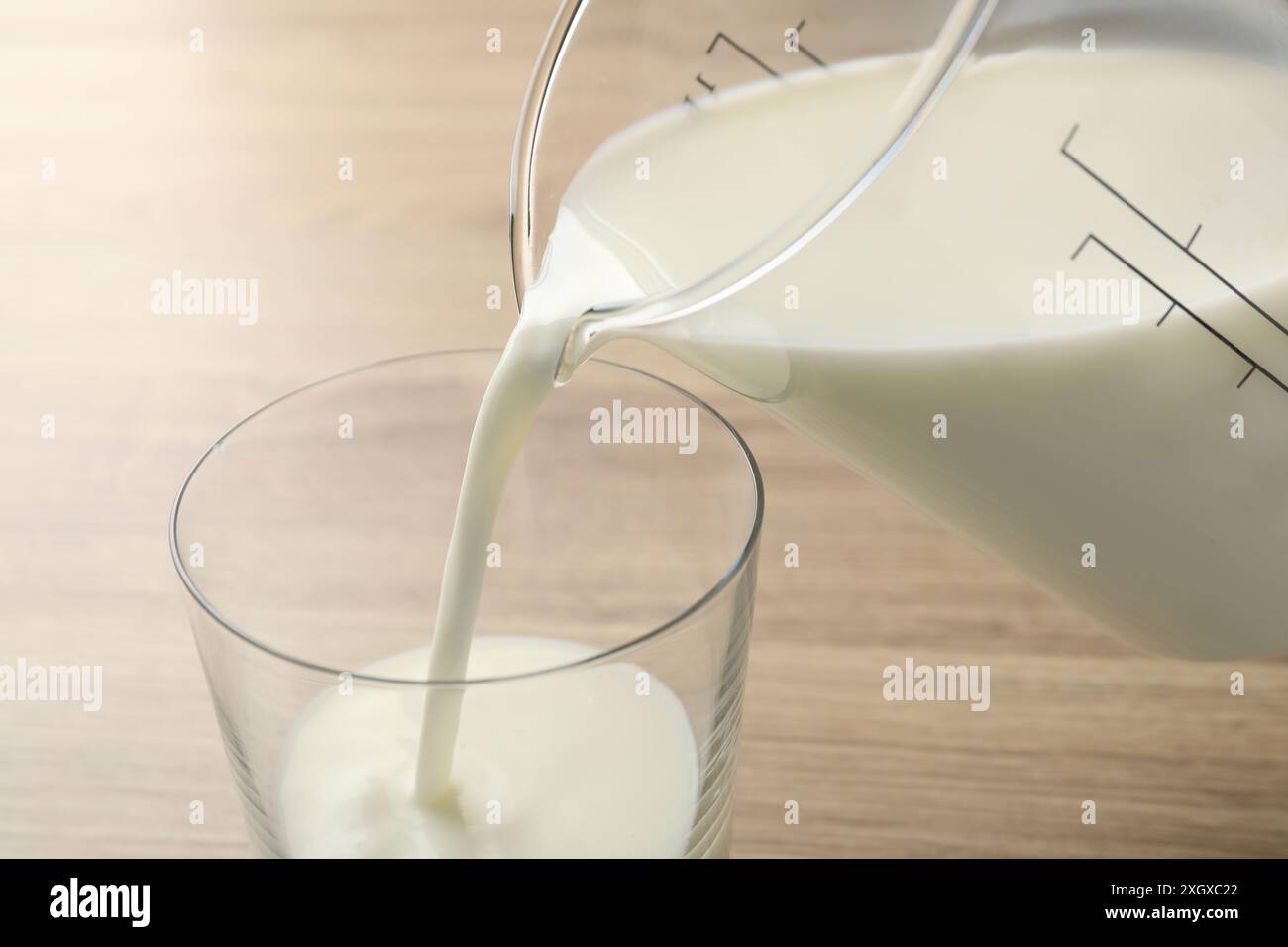 Verser le lait frais de la cruche dans le verre à la table en bois, gros plan Banque D'Images