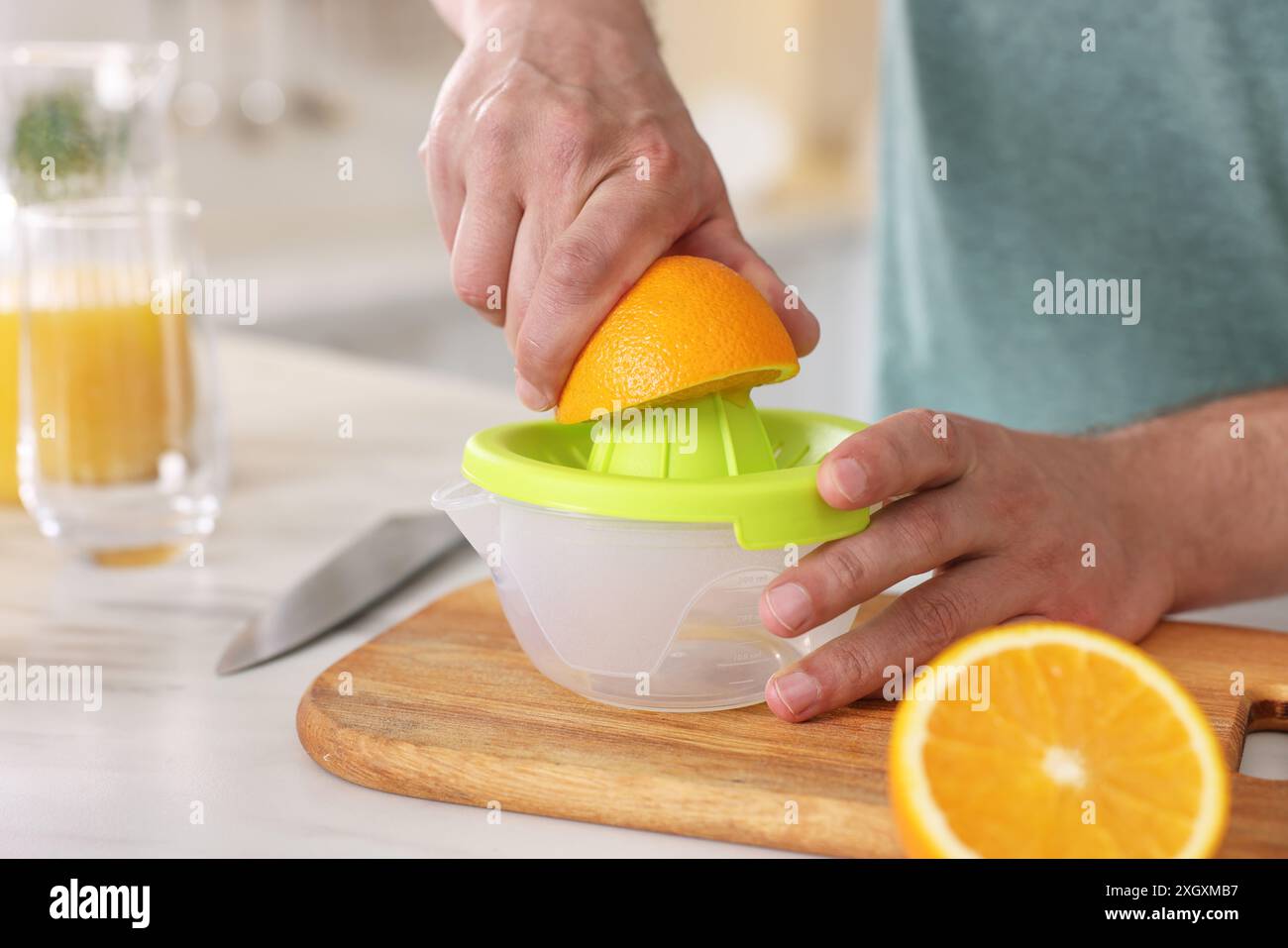 Homme pressant l'orange fraîche avec presse-agrumes à la table blanche dans la cuisine, gros plan Banque D'Images