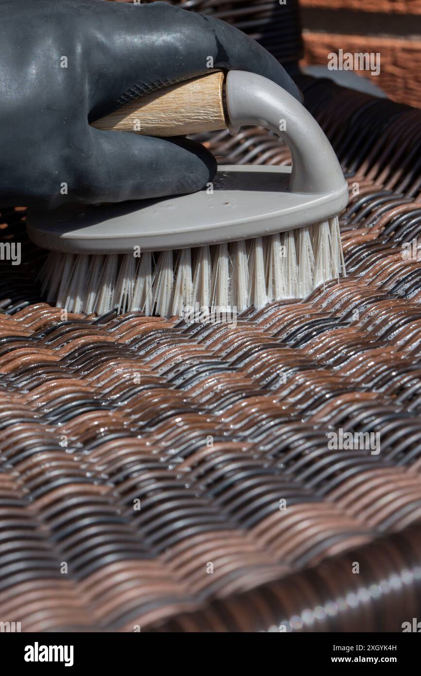 Personne frottant une chaise de jardin en rotin avec une brosse à main. Concept de corvée de travail ménager à la maison de jardin. Banque D'Images