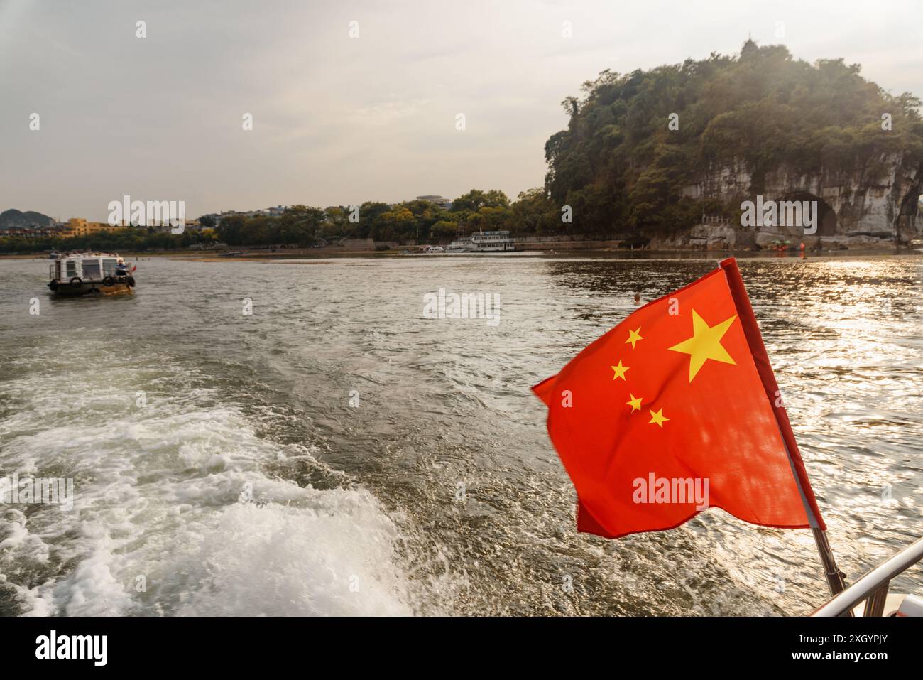Le drapeau de la République populaire de Chine (le drapeau rouge cinq étoiles) flottant sur un bateau naviguant sur la rivière Li au centre-ville de Guilin au coucher du soleil. Banque D'Images