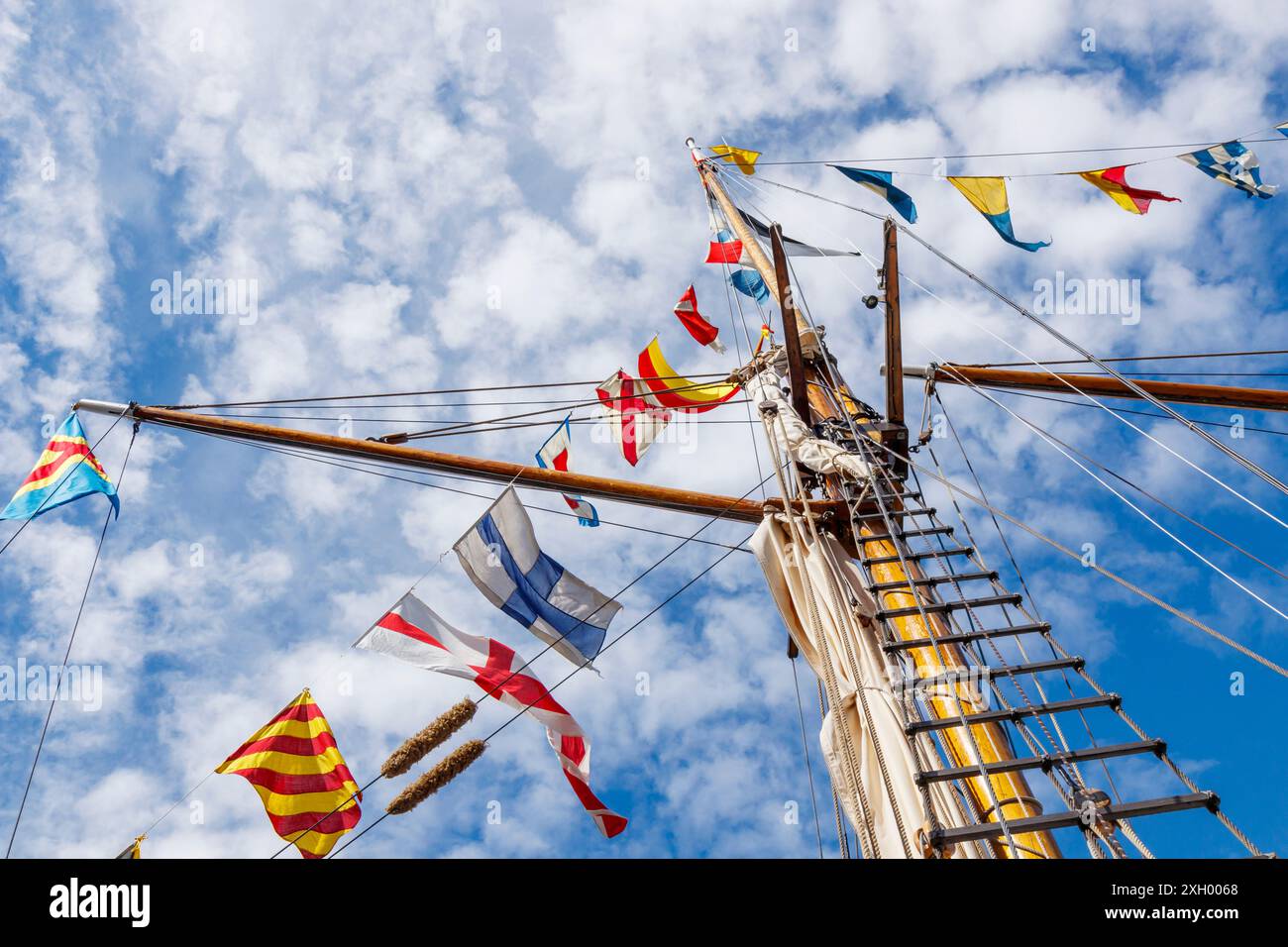 Mât de voilier avec drapeau nautique volant célébration décoration dans un ciel bleu ensoleillé et nuages, gréement de vieux grand voilier avec bu coloré Banque D'Images