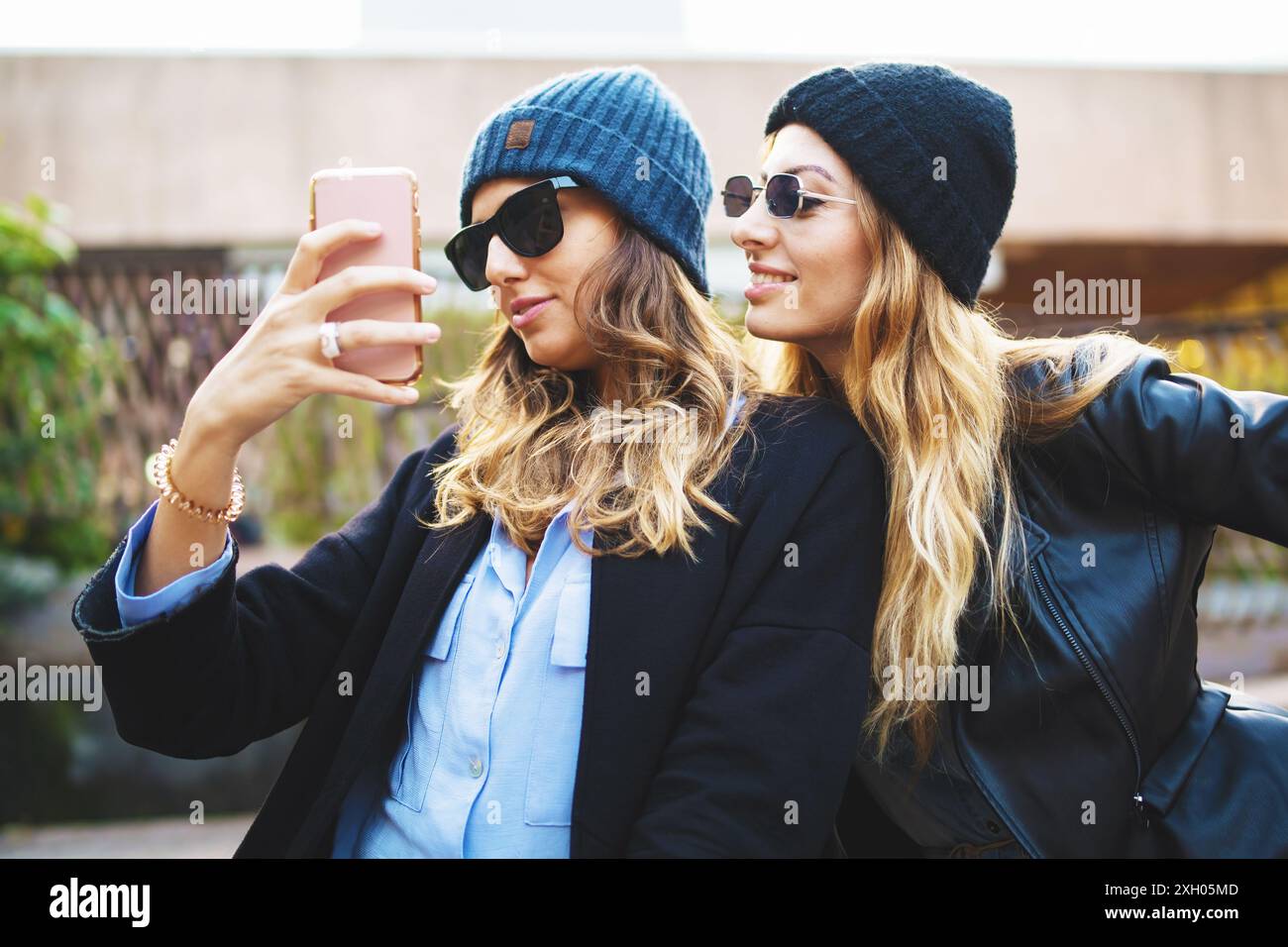 Deux jeunes femmes en tenue d'hiver prenant selfie à l'extérieur. Amis partageant des moments sur les réseaux sociaux, un style de vie urbain, un look avant-gardiste. Exprès joyeux Banque D'Images