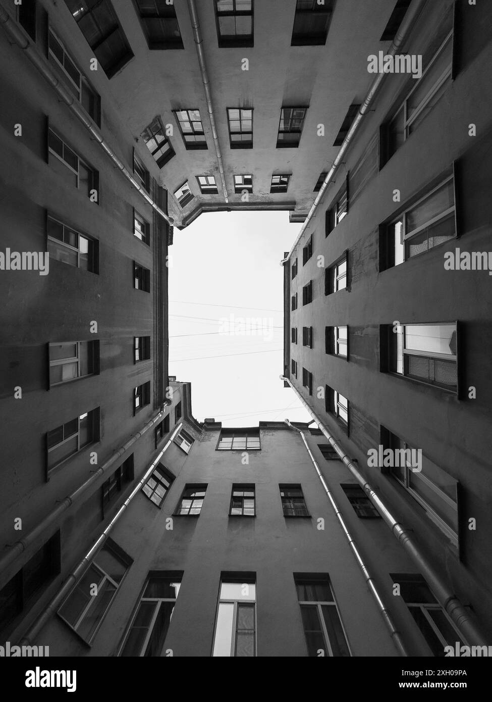 Image en noir et blanc de bâtiments de grande hauteur avec des fenêtres, formant une cour fermée dans un cadre urbain. Perspective à faible angle spectaculaire. Banque D'Images Image en noir et blanc de bâtiments de grande hauteur avec des fenêtres, formant une cour fermée dans un cadre urbain. Perspective à faible angle spectaculaire. Banque D'Images