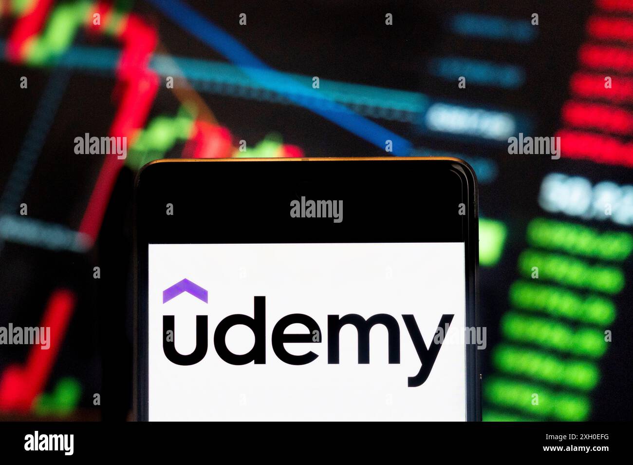 Dans cette illustration photo, le logo de la société de technologie de formation Udemy (NASDAQ : UDMY) vu affiché sur un smartphone avec un graphique de l'indice boursier économique en arrière-plan. Banque D'Images