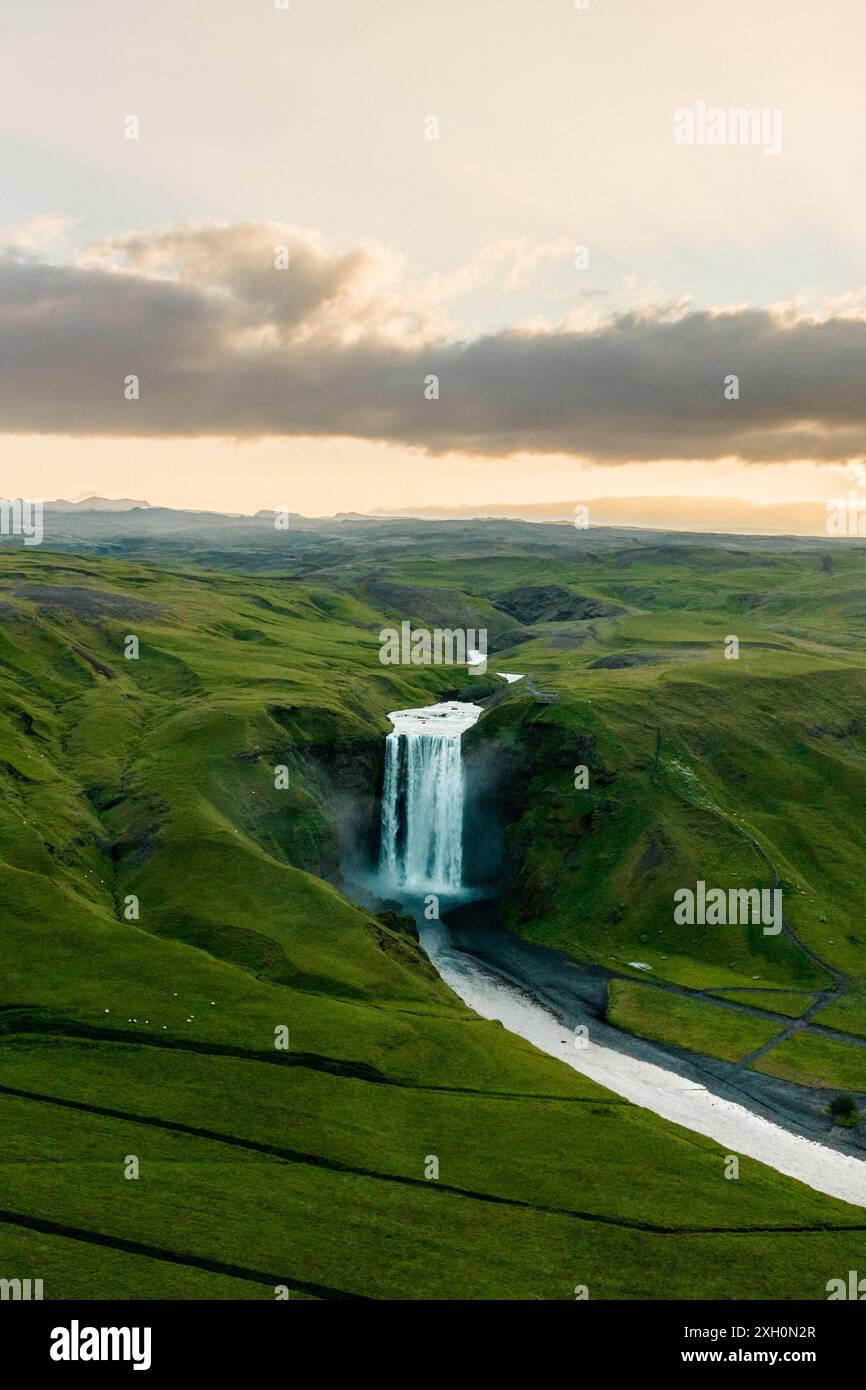Vue aérienne de la cascade de Skogafoss en Islande au coucher du soleil, entourée de paysages verdoyants et d'un ciel spectaculaire. Banque D'Images