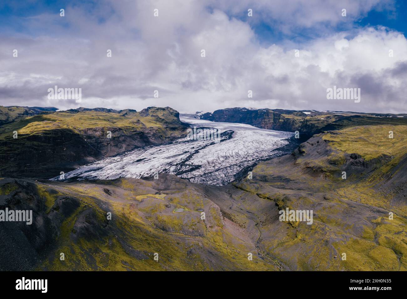 Vue aérienne du glacier Solheimajokull en Islande, avec des montagnes vertes et vibrantes couvertes de mousse contrastant avec le glacier blanc Banque D'Images