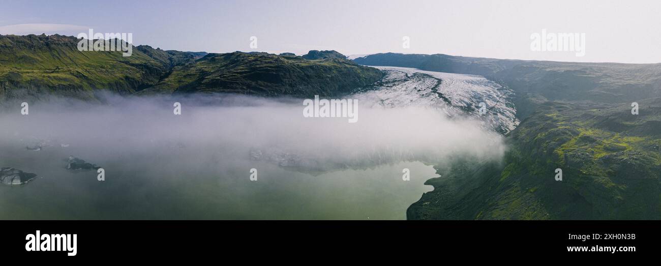 Une vue aérienne panoramique du glacier Sólheimajokull en Islande, avec des montagnes verdoyantes, un lagon glaciaire et une couche de brume. Banque D'Images